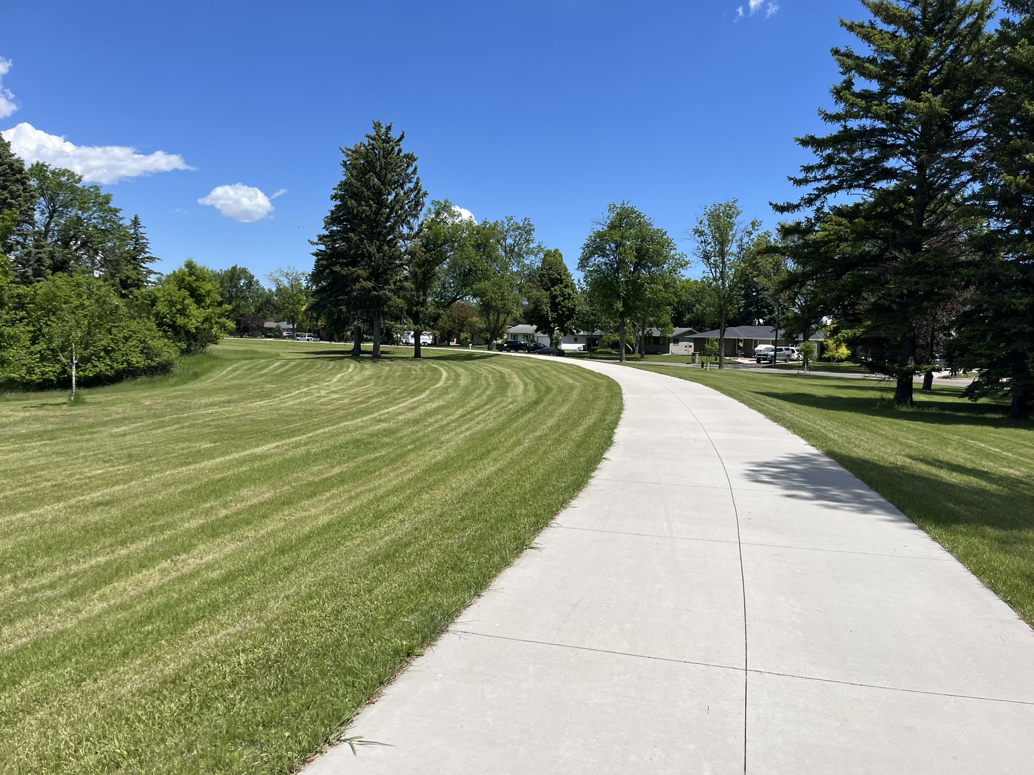 Paved path winding through green grass and trees under a clear blue sky. - Fargo to Sabin loop