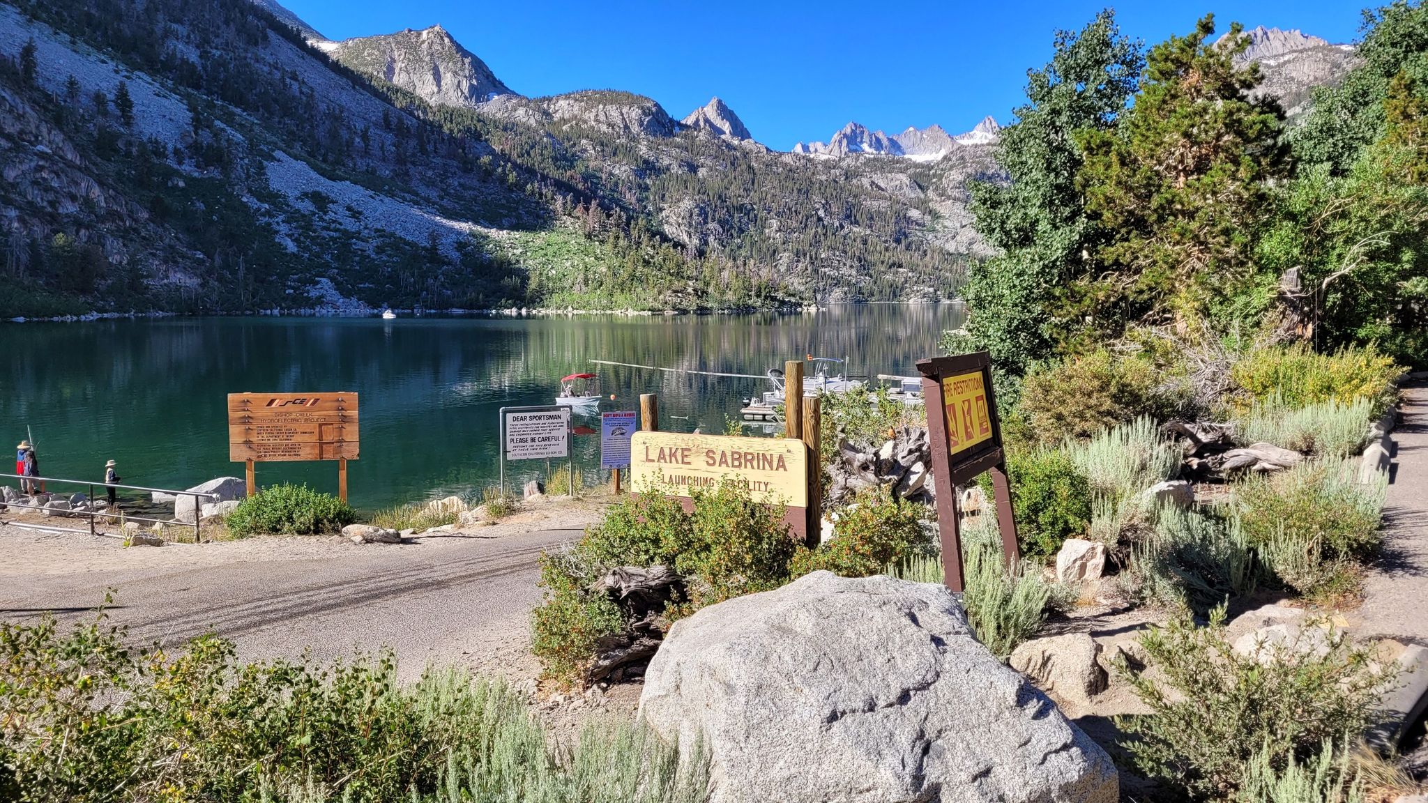 Sunny mountain lake with signs, a dock, and distant peaks under clear sky. - Lake Sabrina