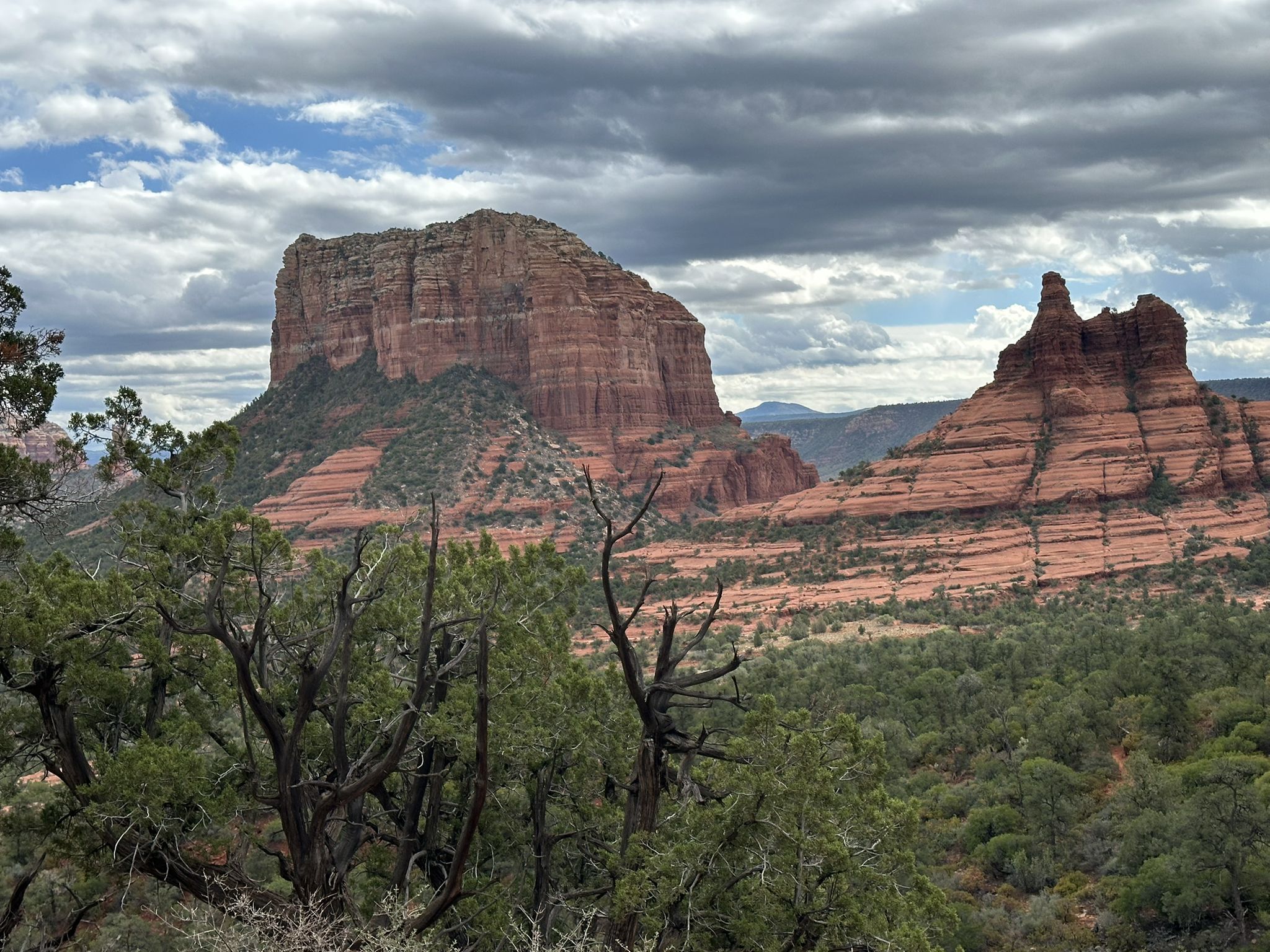 Red rock mountains and green trees under a dramatic cloudy sky. - Yavapai Vista and Slim Shady Loop