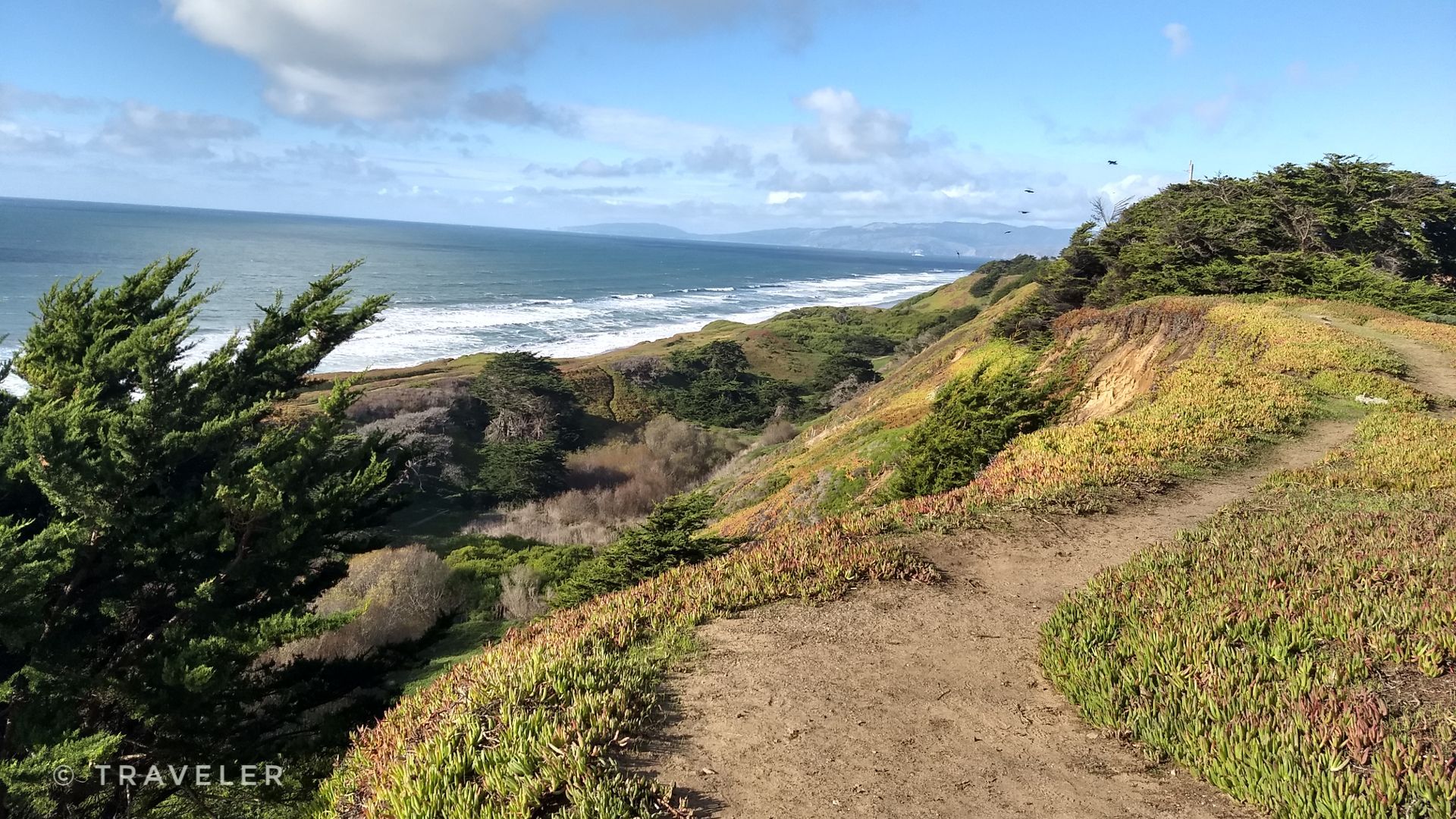 Dirt path on a green hillside overlooking the ocean with crashing waves. - Thornton Beach Trail