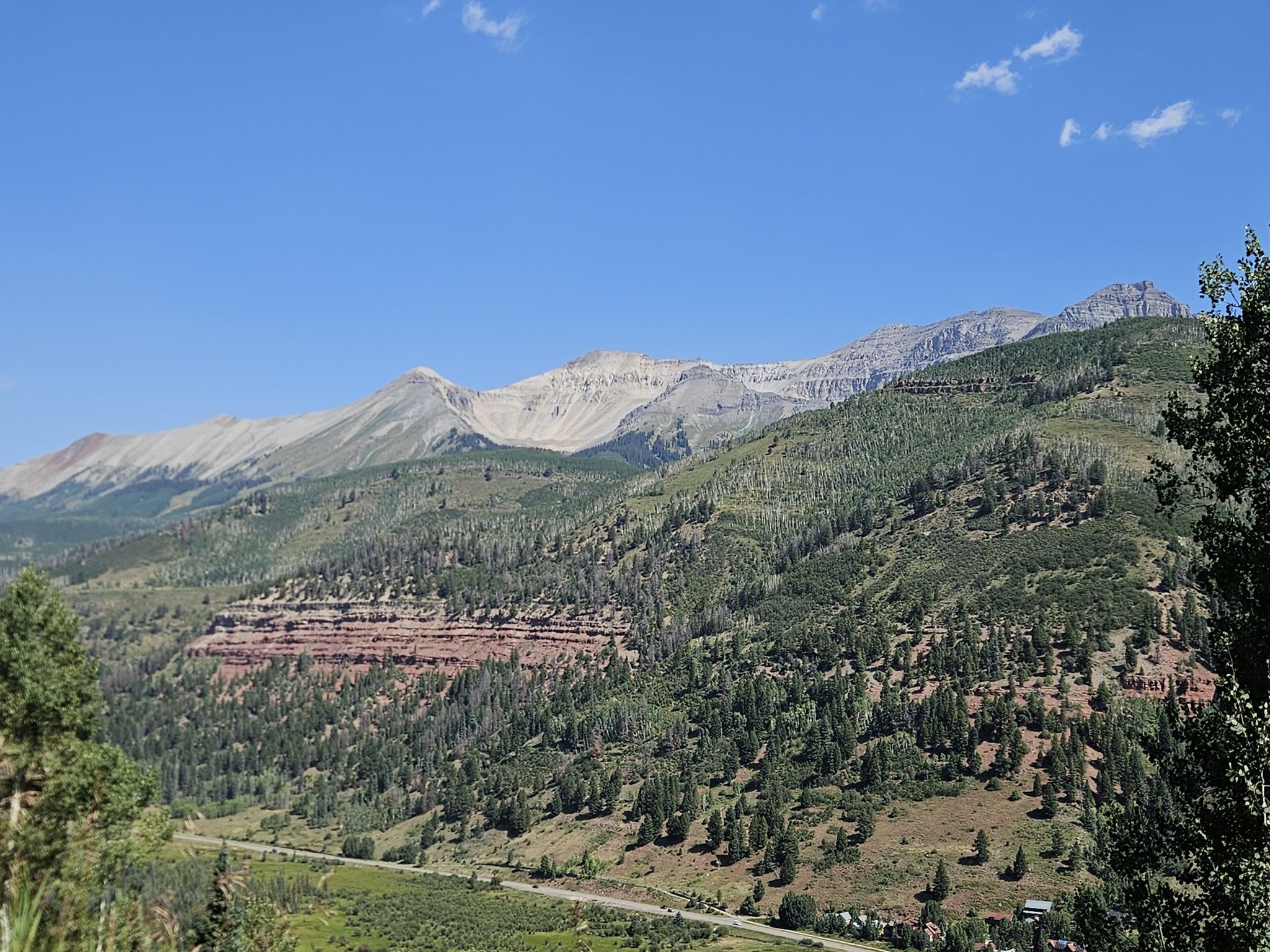 Vast mountain landscape with green forests, red rock, and a winding road. - See Forever Road to Gold Hill