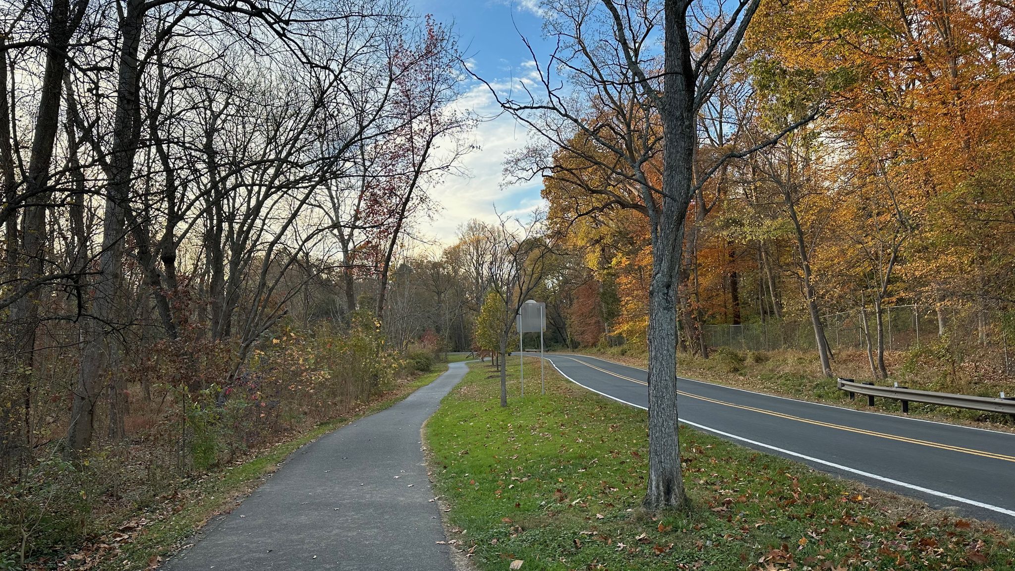 A paved path runs parallel to a road, flanked by autumn trees. - Query Mill & Glen Road – Meadowbrook Stables loop from Fort Totten