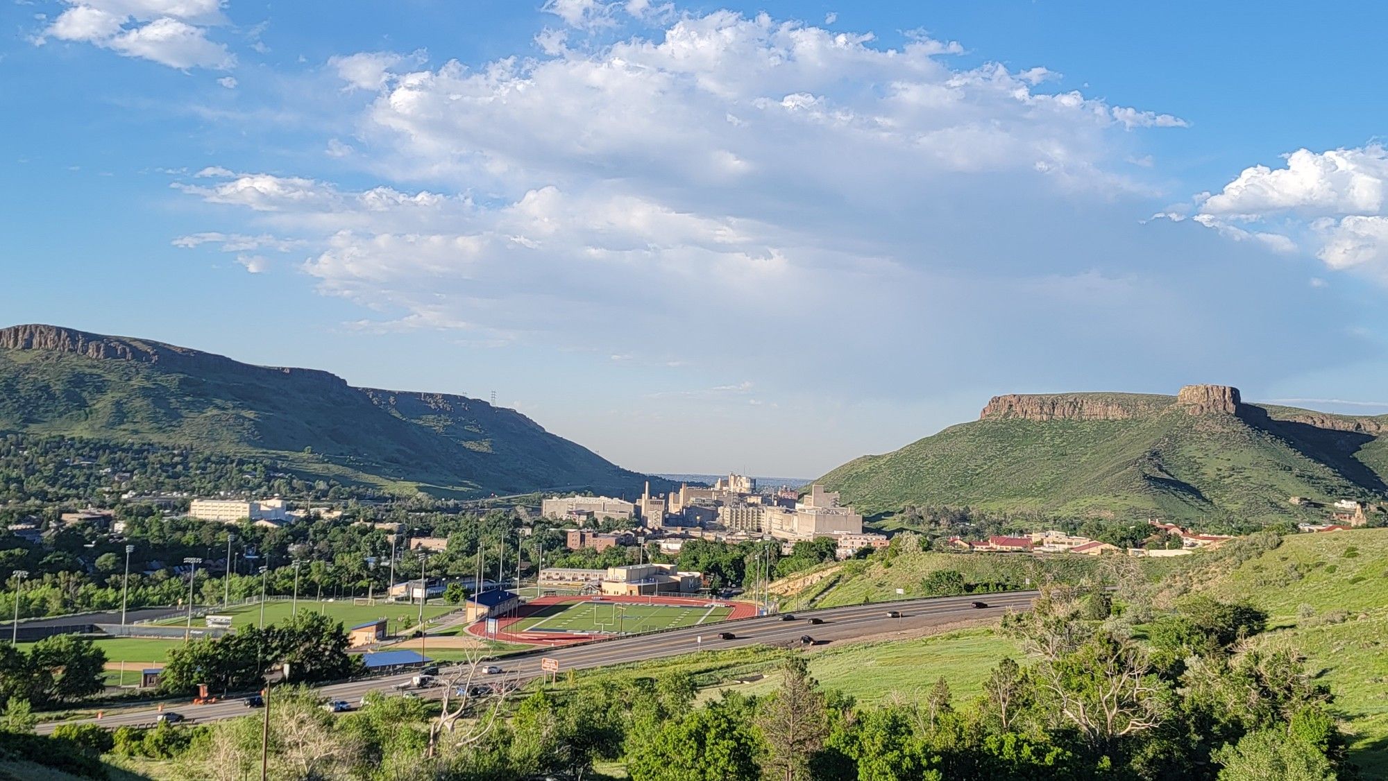 A town in a green valley between mountains under a bright, cloudy sky. - Chimney Gulch Trail