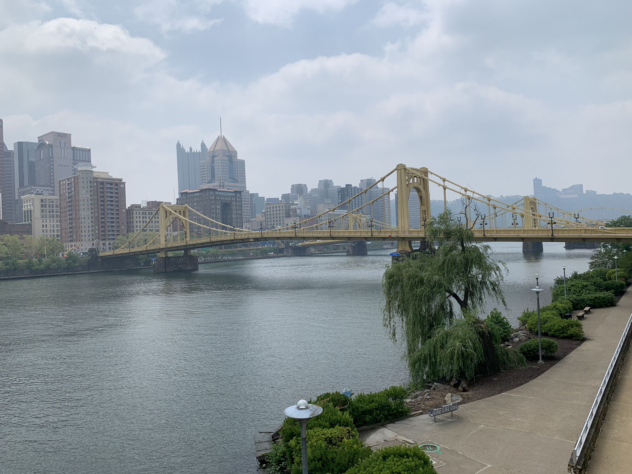 Yellow bridge over a river, city skyline, and a park path under cloudy skies. - Andy Warhol Bridge – View of the Andy Warhol Bridge loop from Tree of Life Or L'Simcha Congregation