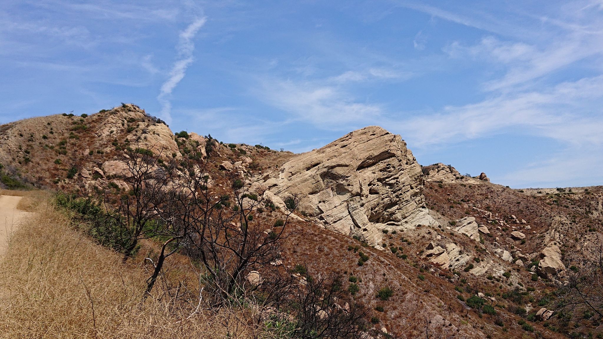 A dirt path winds through dry, rocky hills under a bright blue sky. - Eagle Springs Fire Road