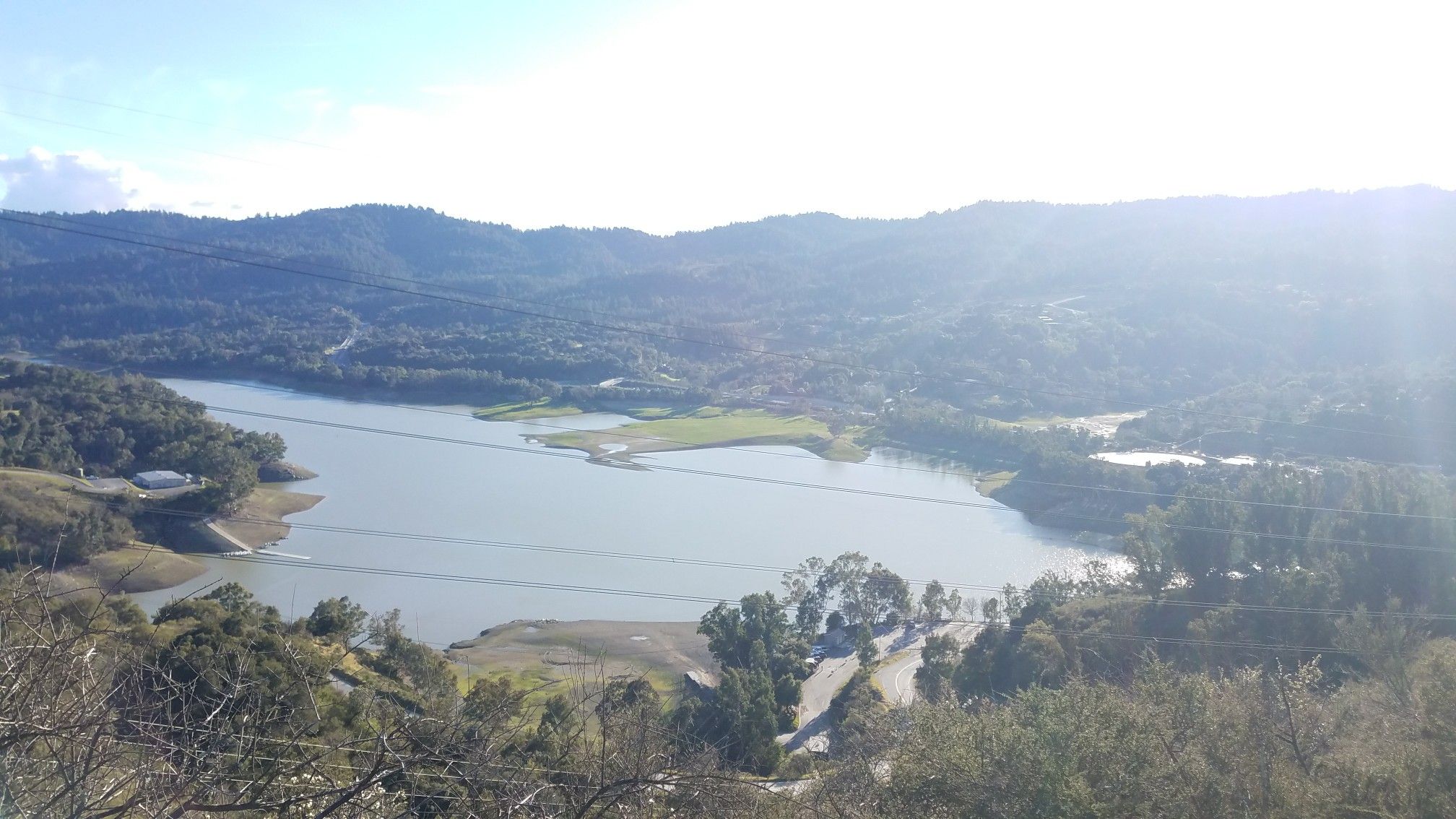 Sunny lake and forested hills with bright lens flare. - Lexington Reservoir Overlook – Saint Josephs Hill summit loop from Los Gatos