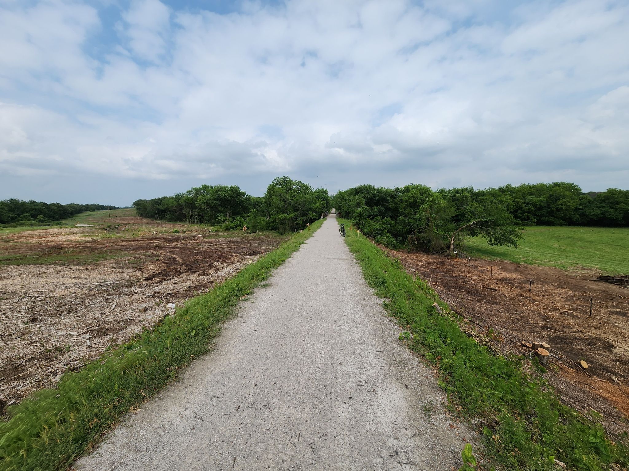 A straight dirt path through cleared land and green trees under a cloudy sky. - Lake Mineral Wells State Trailway Loop