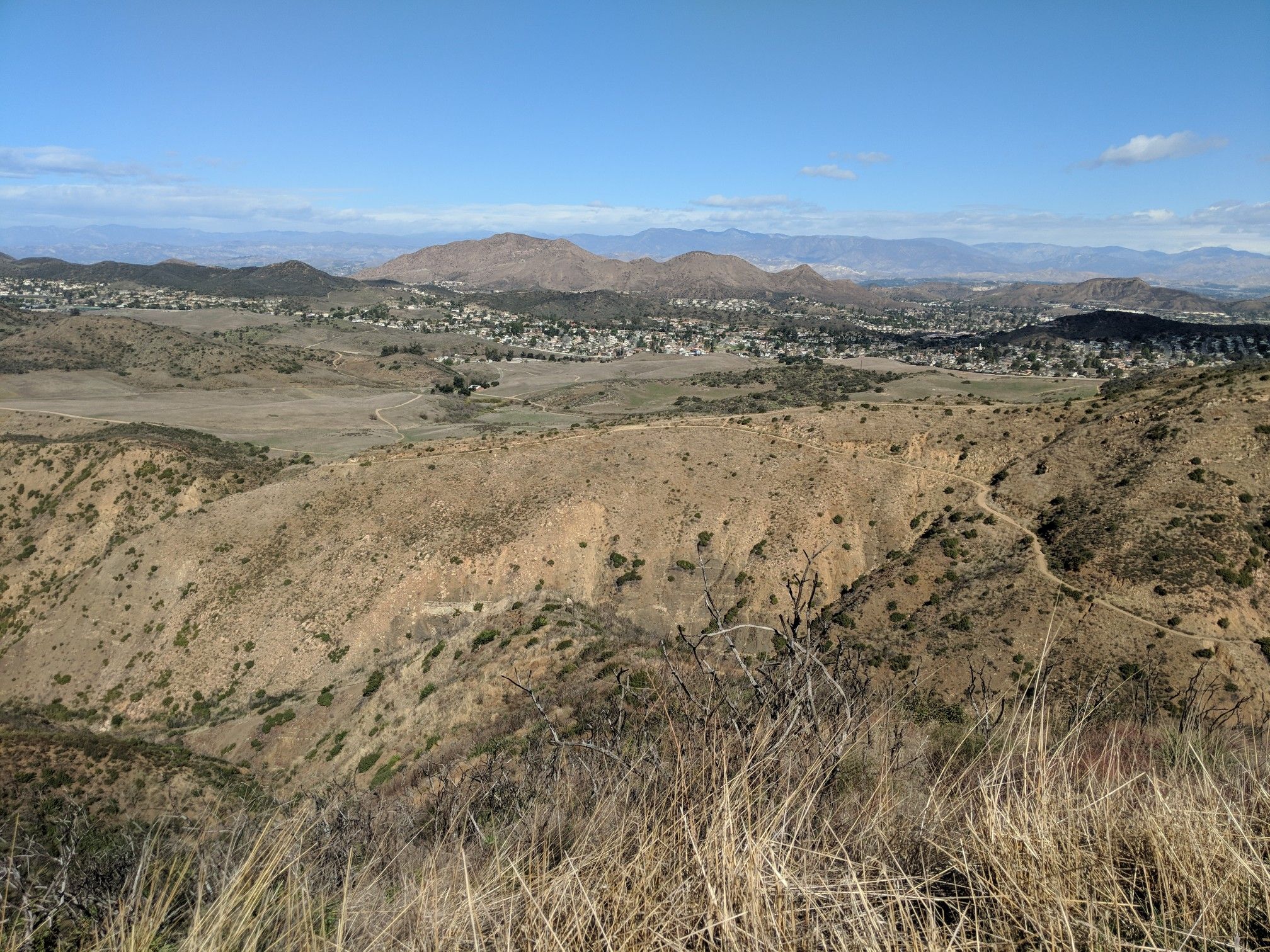 Expansive view of dry, rolling hills and a distant town under clear sky. - Satwiwa Loop and Upper Cabin Trail