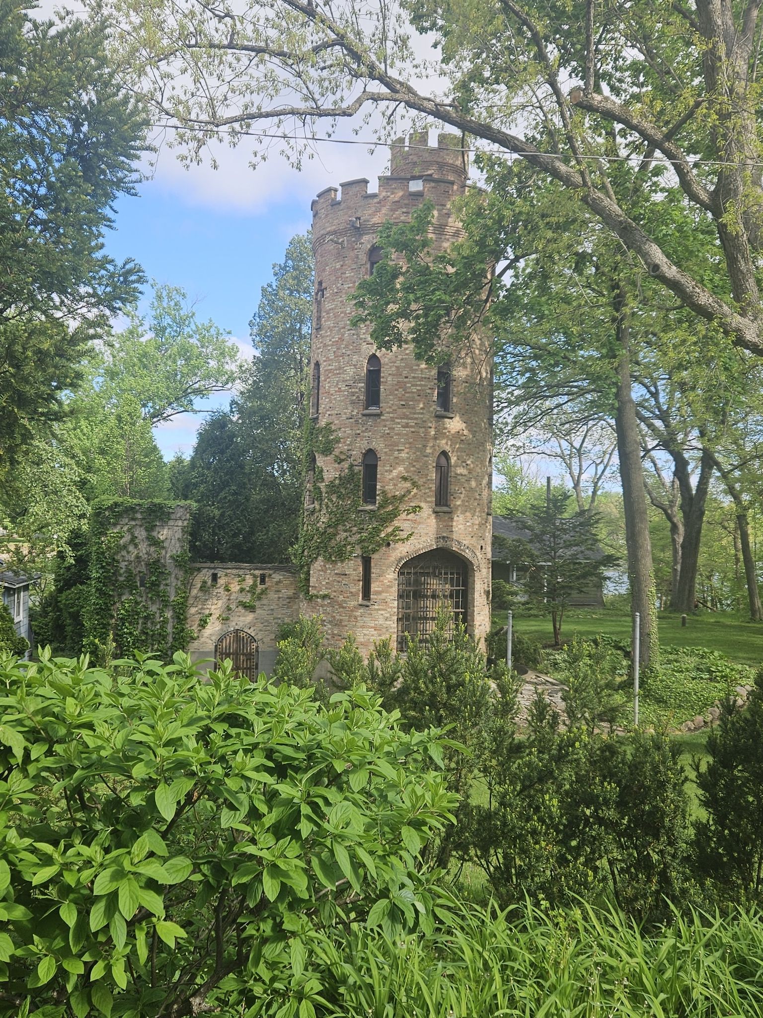 A stone tower with ivy, surrounded by green trees under a bright sky. - Fox River – Pratt's Castle loop from Elgin