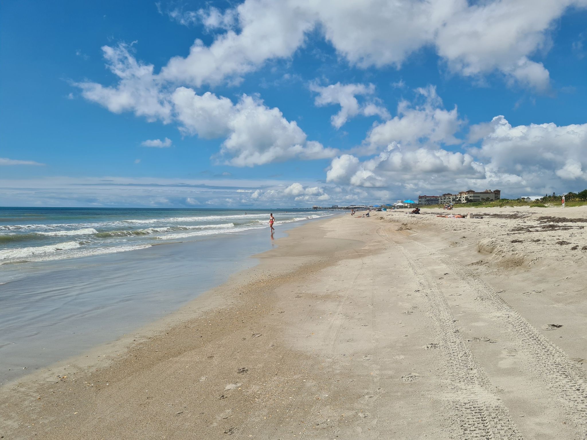 Sunny beach with ocean waves, a person walking, and fluffy clouds. - Cocoa Beach Pier loop from Four Islands