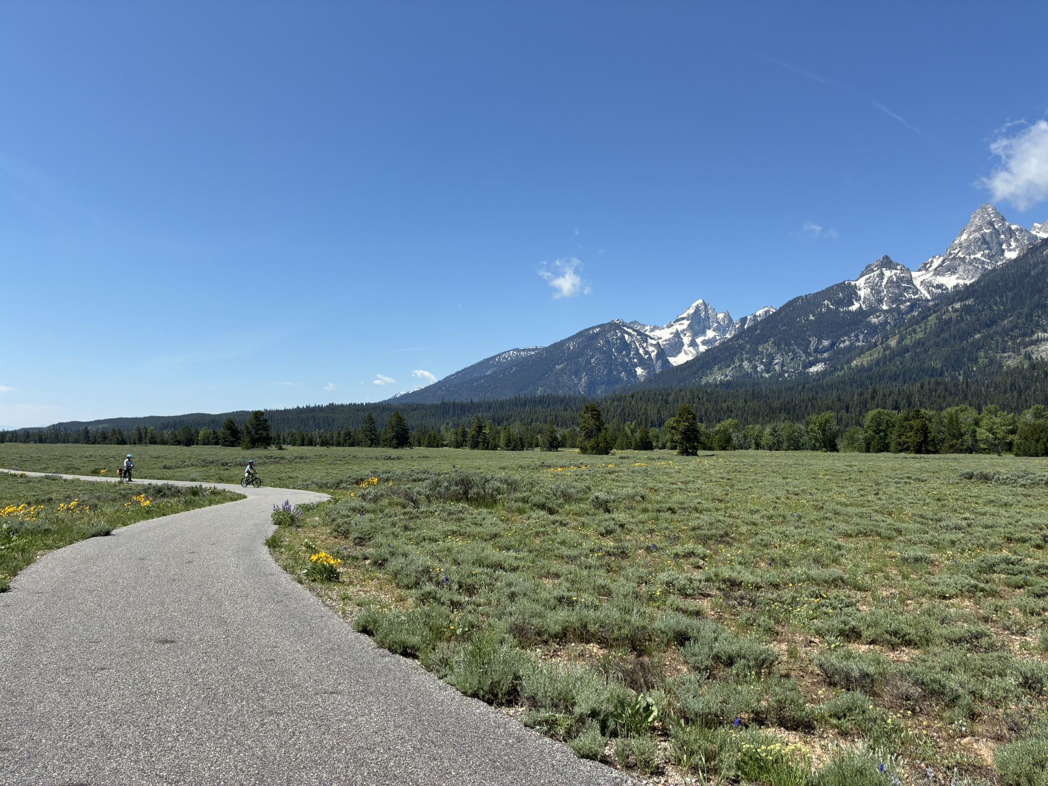 Two cyclists on a paved path through a meadow with mountains. - Snake Lake Loop Trail