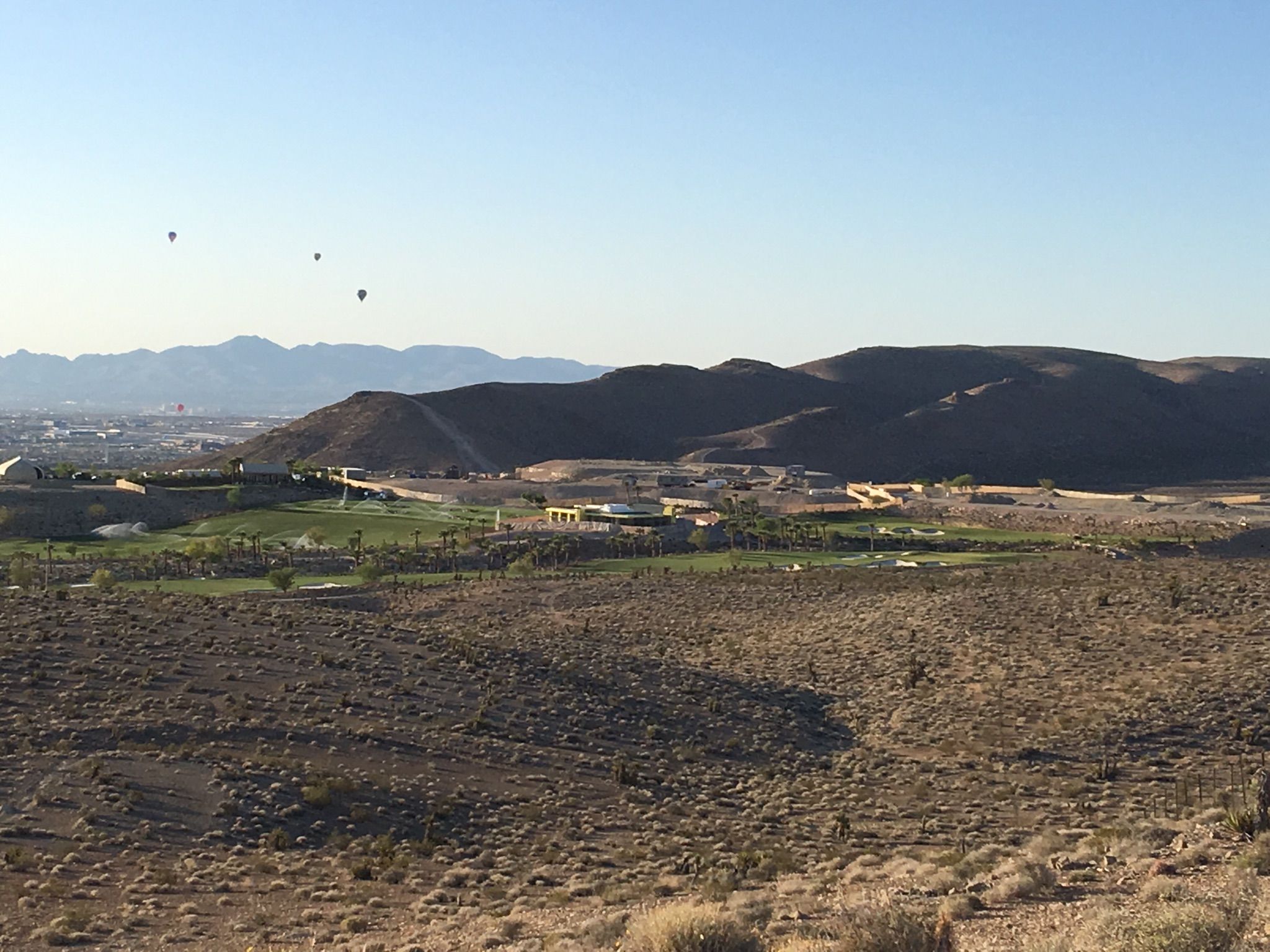 Desert landscape with a golf course, buildings, and hot air balloons. - Bear's Best loop — Bears Best
