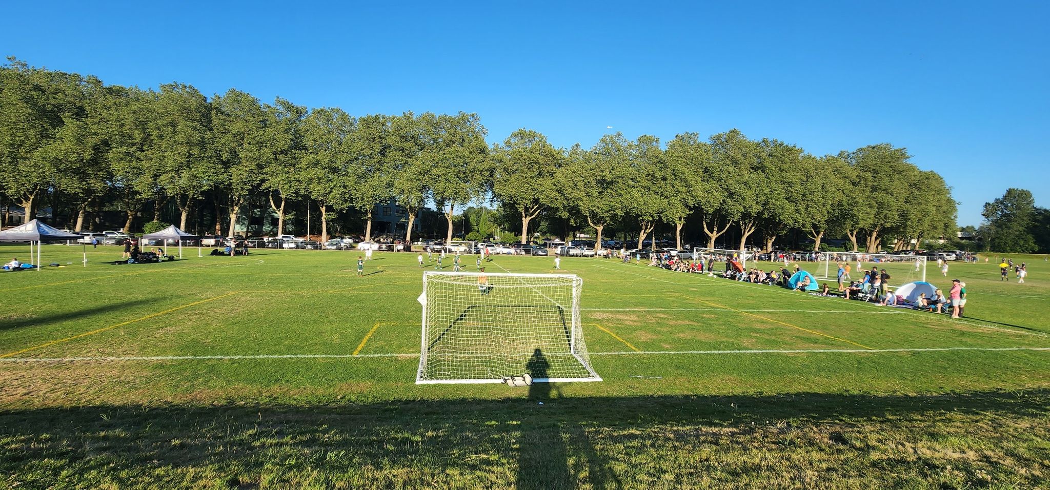 A soccer goal on a sunny green field with people gathered in the background. - Green River Trail: Tukwila Section