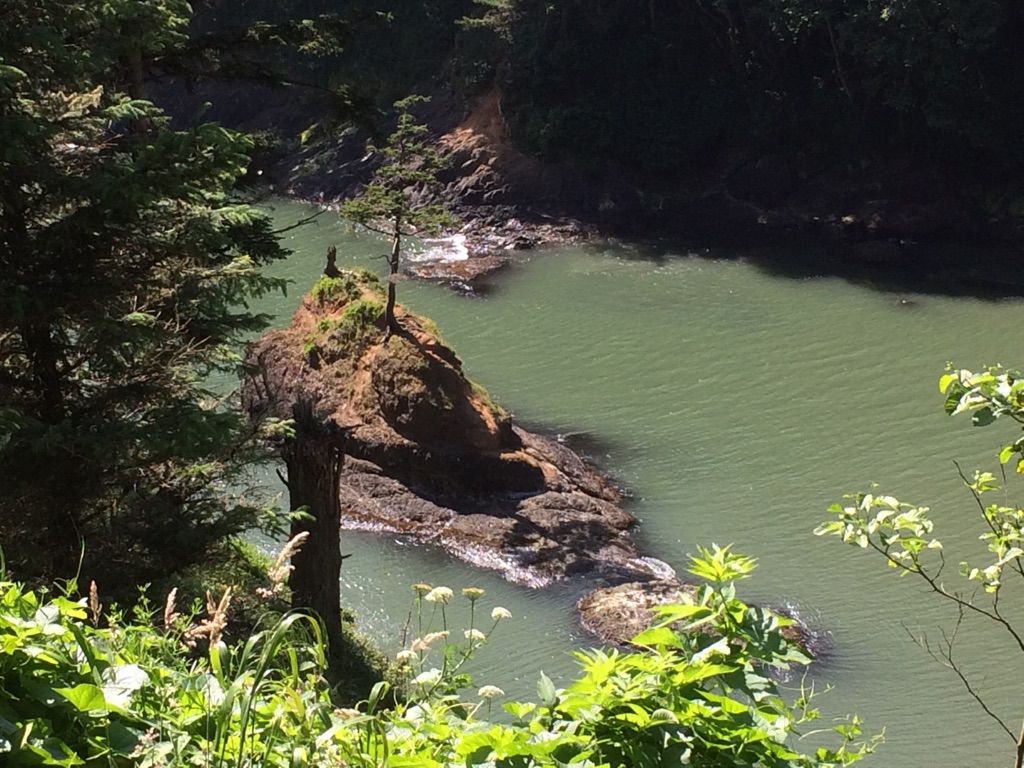 Sunny aerial view of a small rocky island in green coastal water. - Cape Disappointment Trail