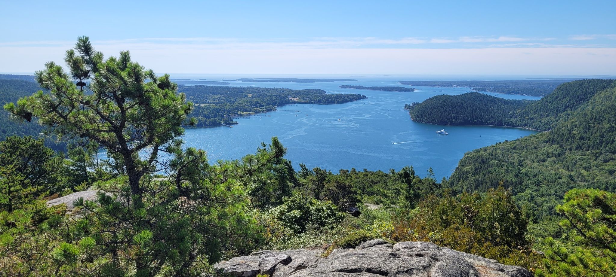 Panoramic view of a blue bay with islands, forested hills, and a clear sky. - Acadia Mountain Loop
