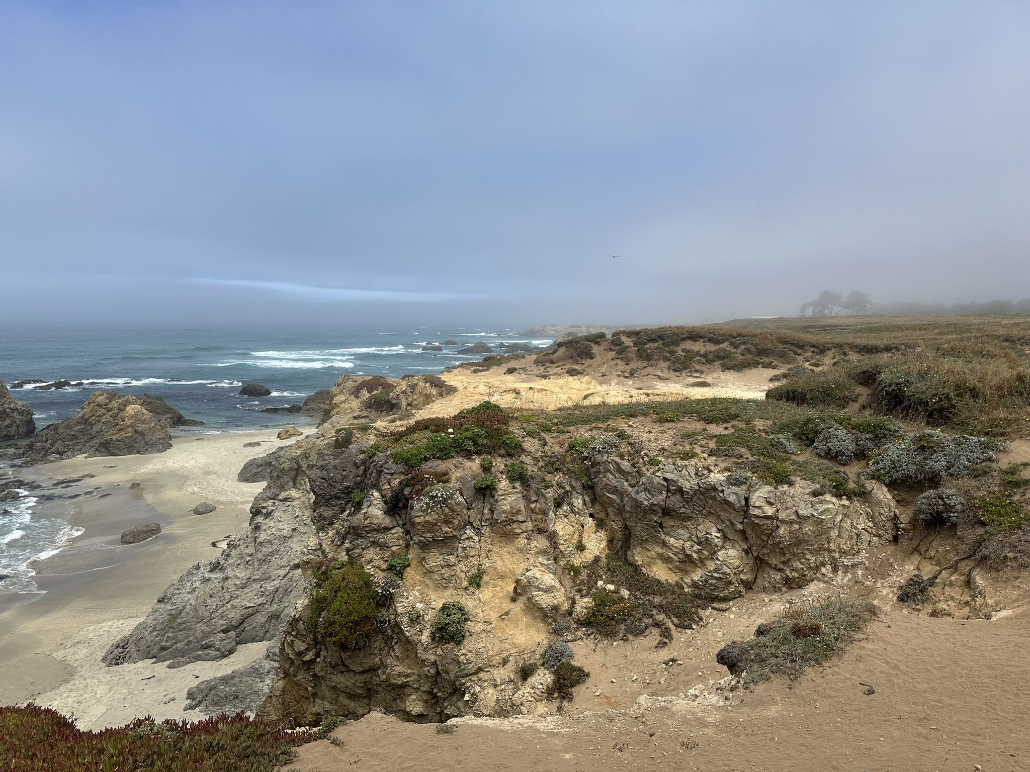 Overcast view of a rocky coastline, sandy beach, and ocean waves. - Ka Kahleh Trail