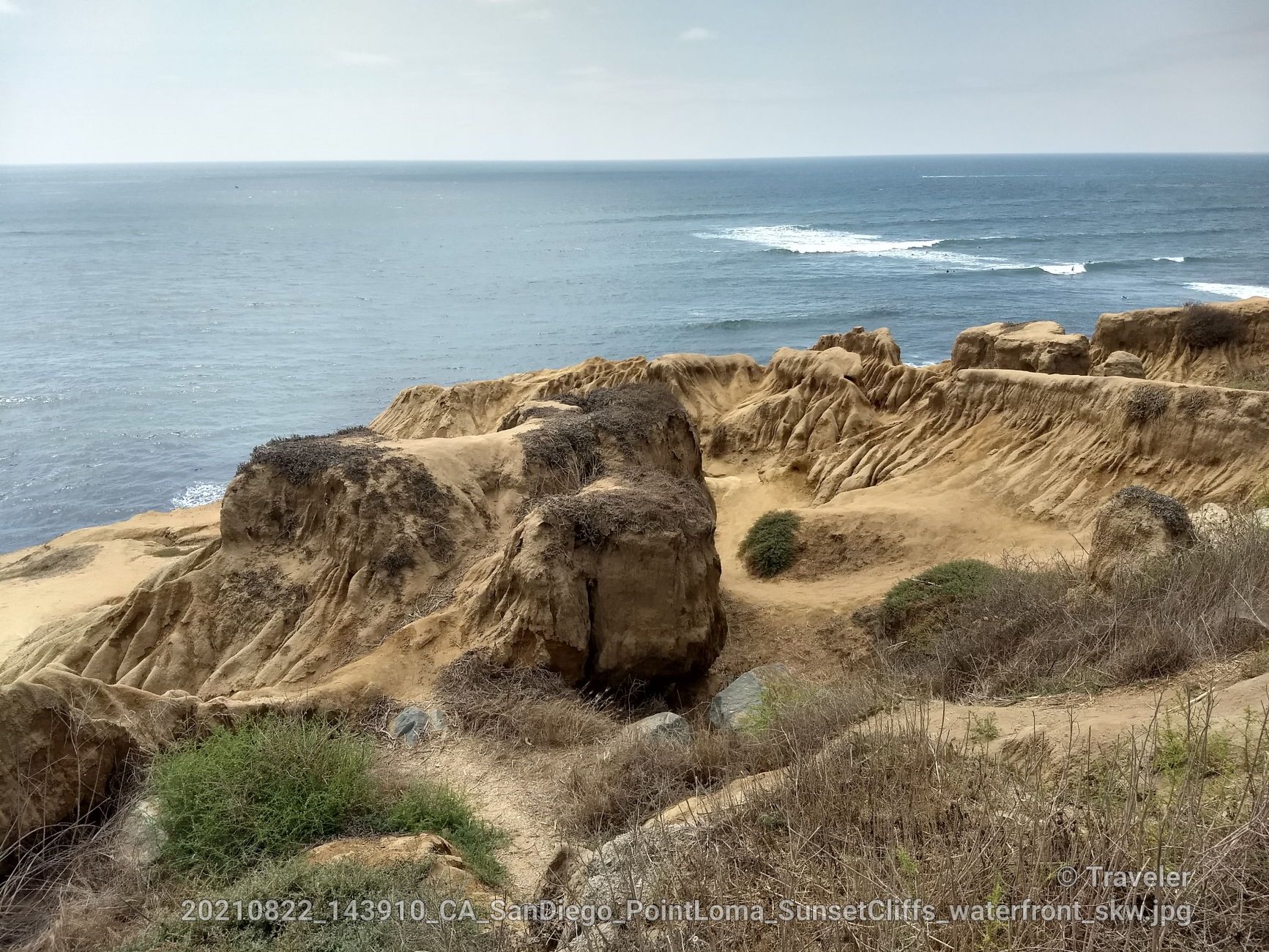 Eroded sandstone cliffs and rock formations meet the ocean under a bright sky. - Sunset Cliffs Loop Trail