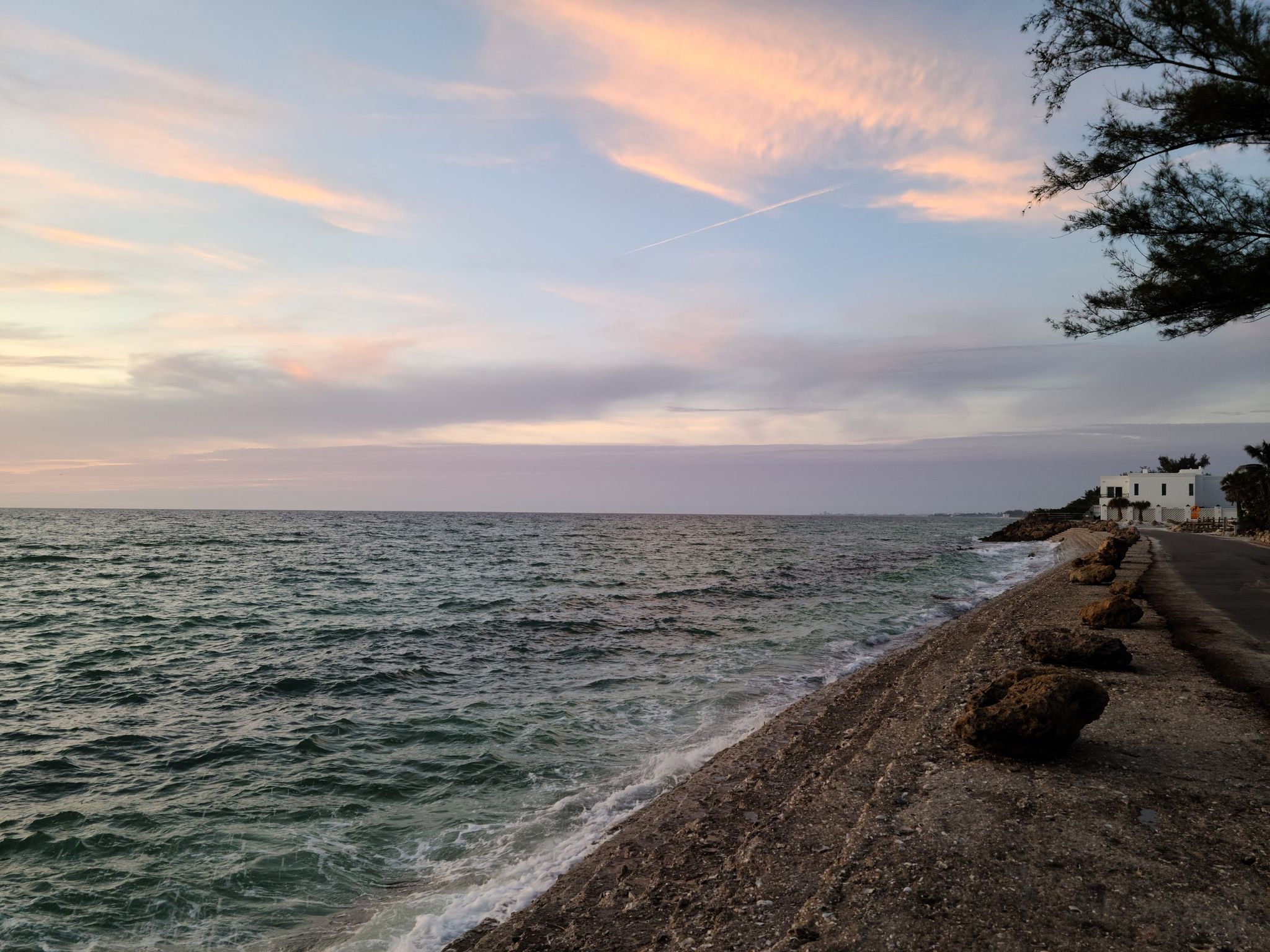 Choppy ocean waves at dusk with pink clouds over a rocky shore and road. - Casey Key Road Scenic Drive