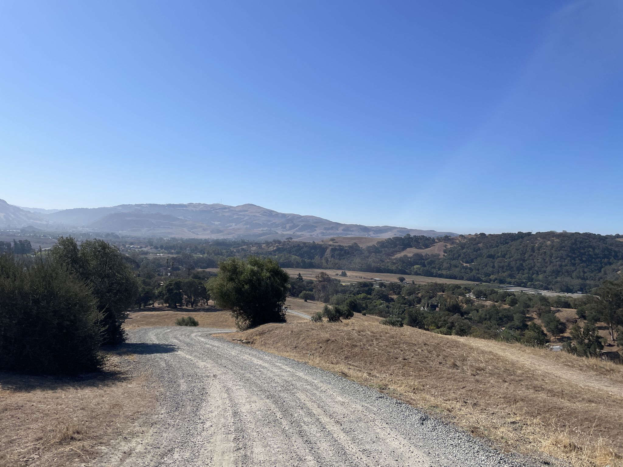 A gravel road winds through dry hills overlooking a green valley. - Sunol Depot loop from Sunol