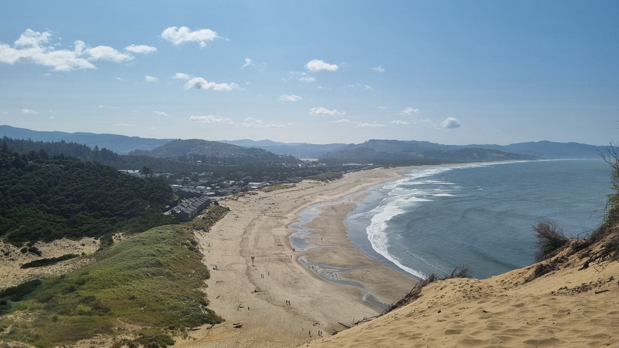Panoramic view of a sunny beach, ocean, coastal town, and distant mountains. - Pelican Pub & Brewery – Cape Kiwanda loop from Pacific City