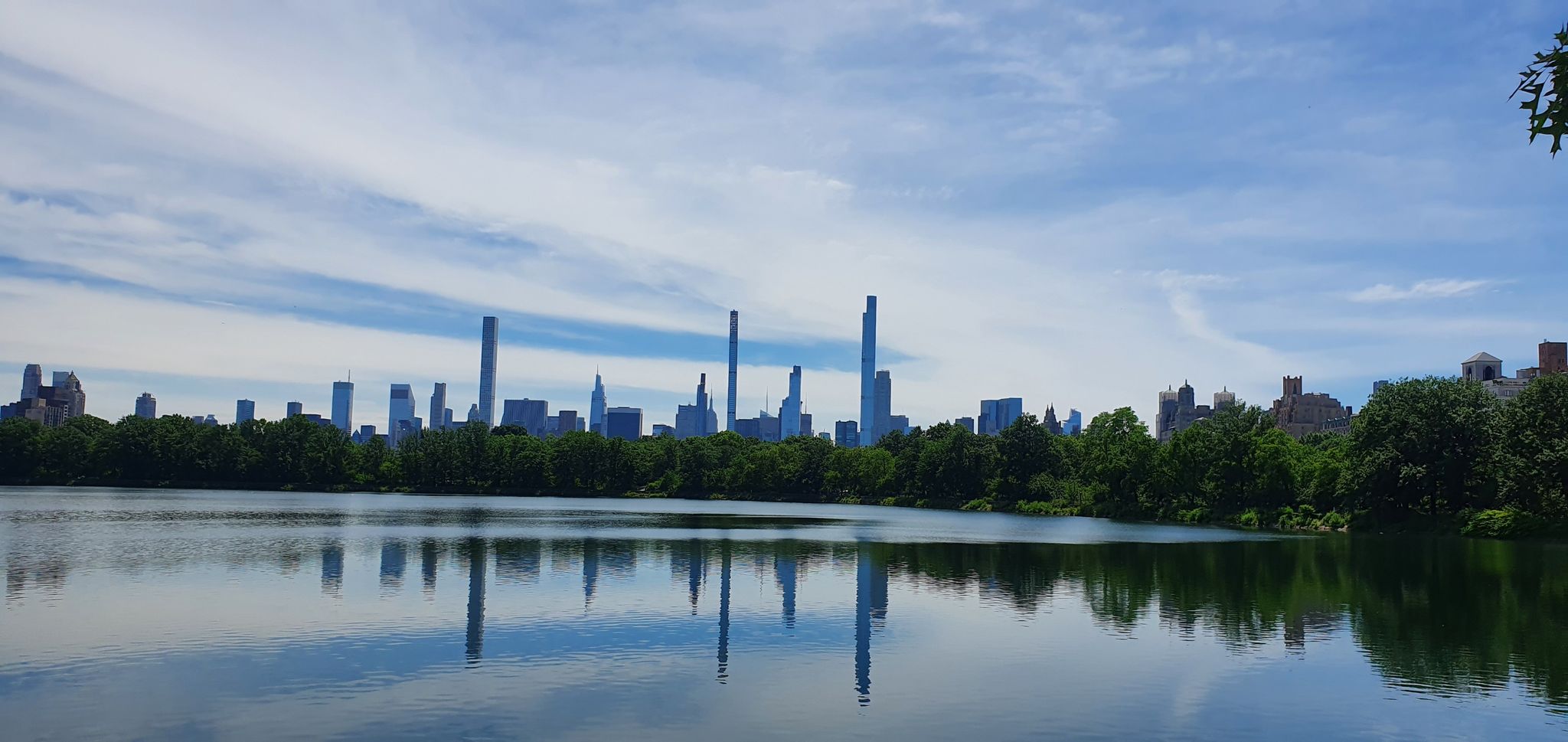 Lake reflecting a distant city skyline under a blue, cloudy sky. - Northwest Central Park Loop