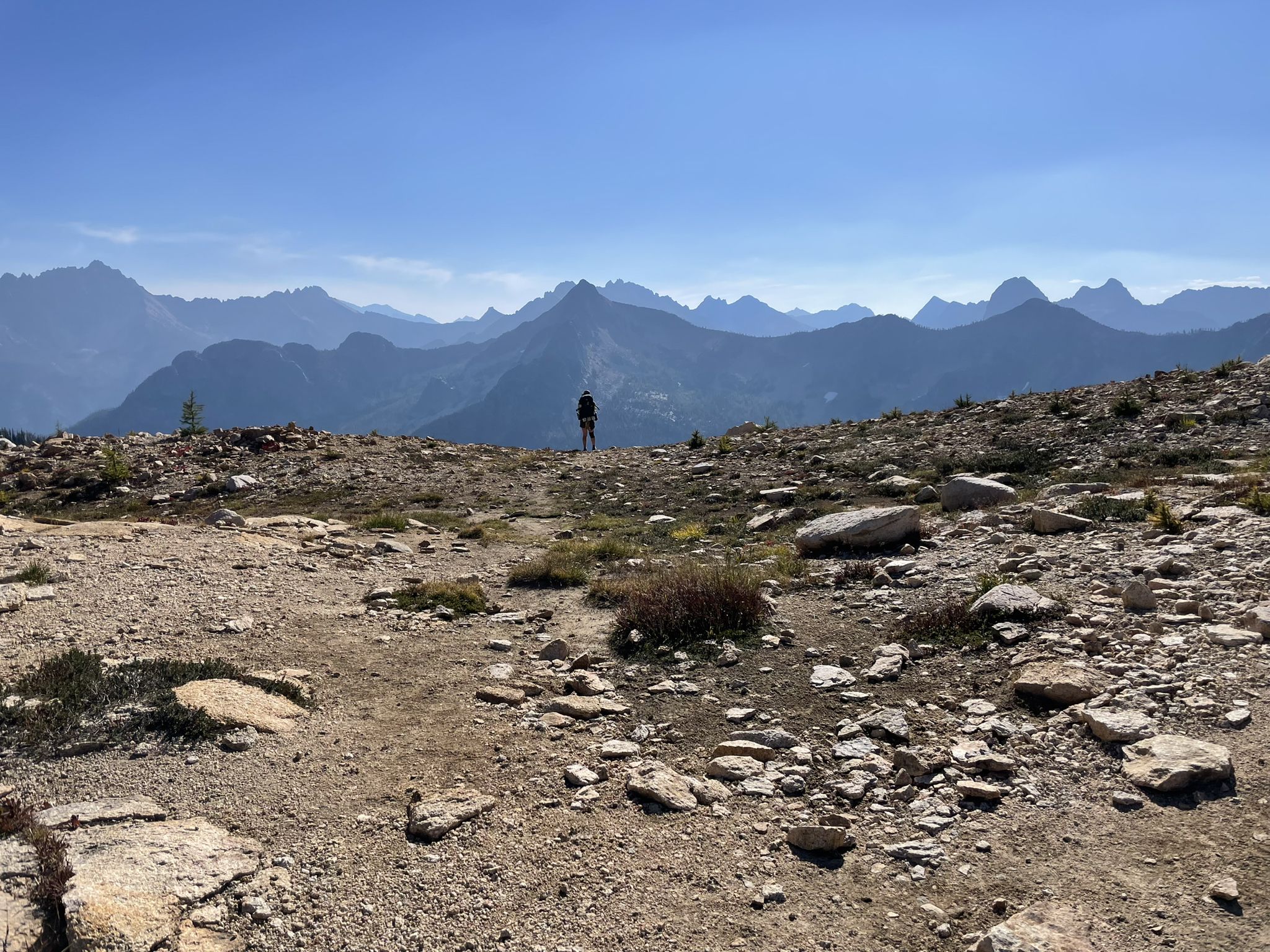 A person stands on a rocky mountain ridge overlooking distant peaks. - Cutthroat Creek Trail