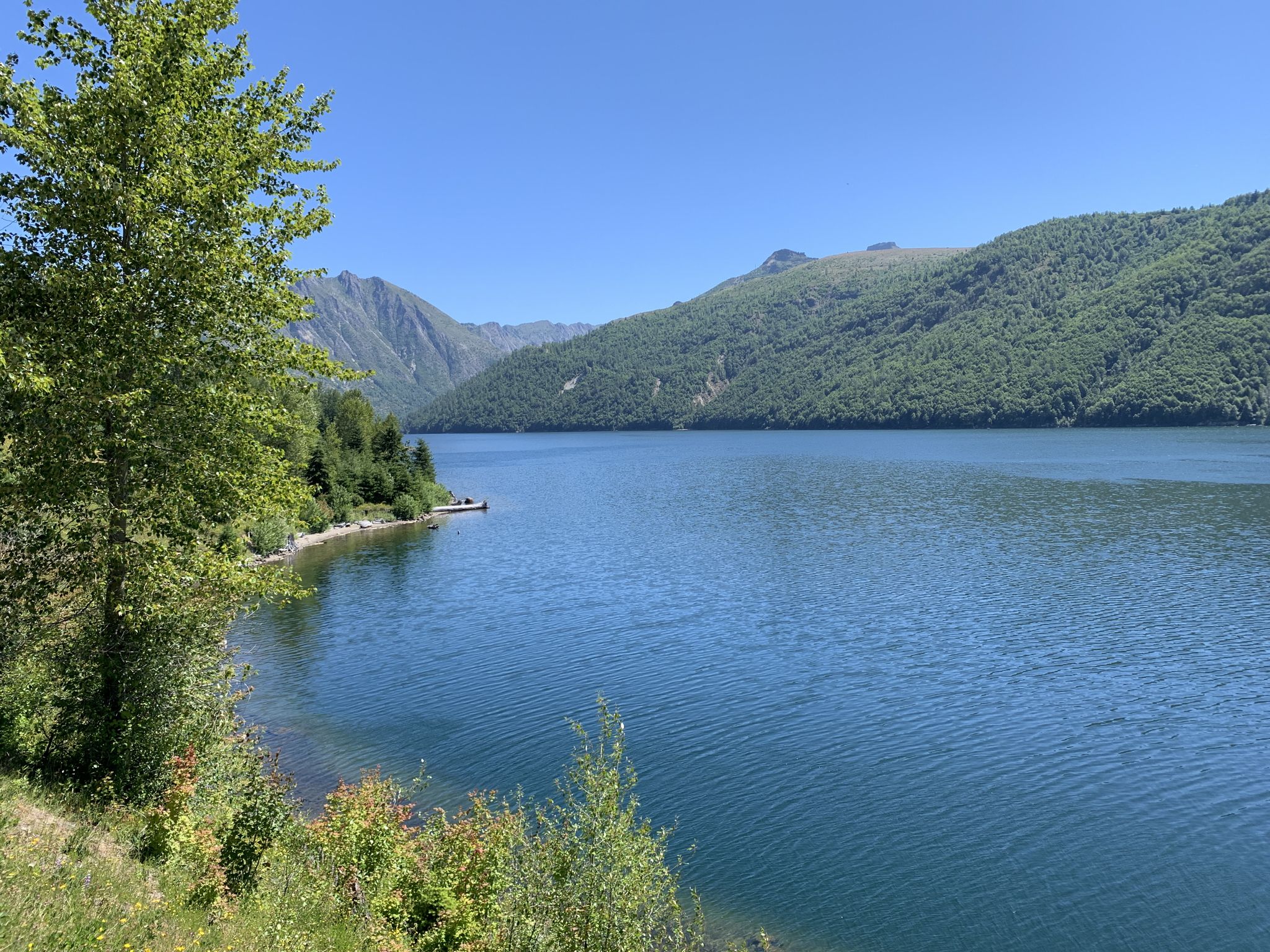 Serene blue lake surrounded by lush green mountains under a clear sky. - Lakes Trail