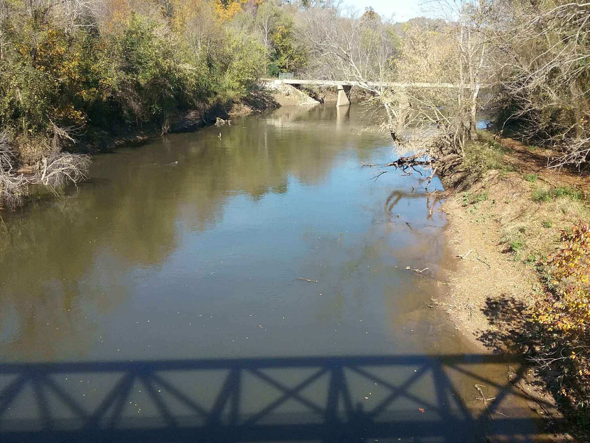 A calm river flows under a distant bridge on a clear autumn day. - Neuse River Trail