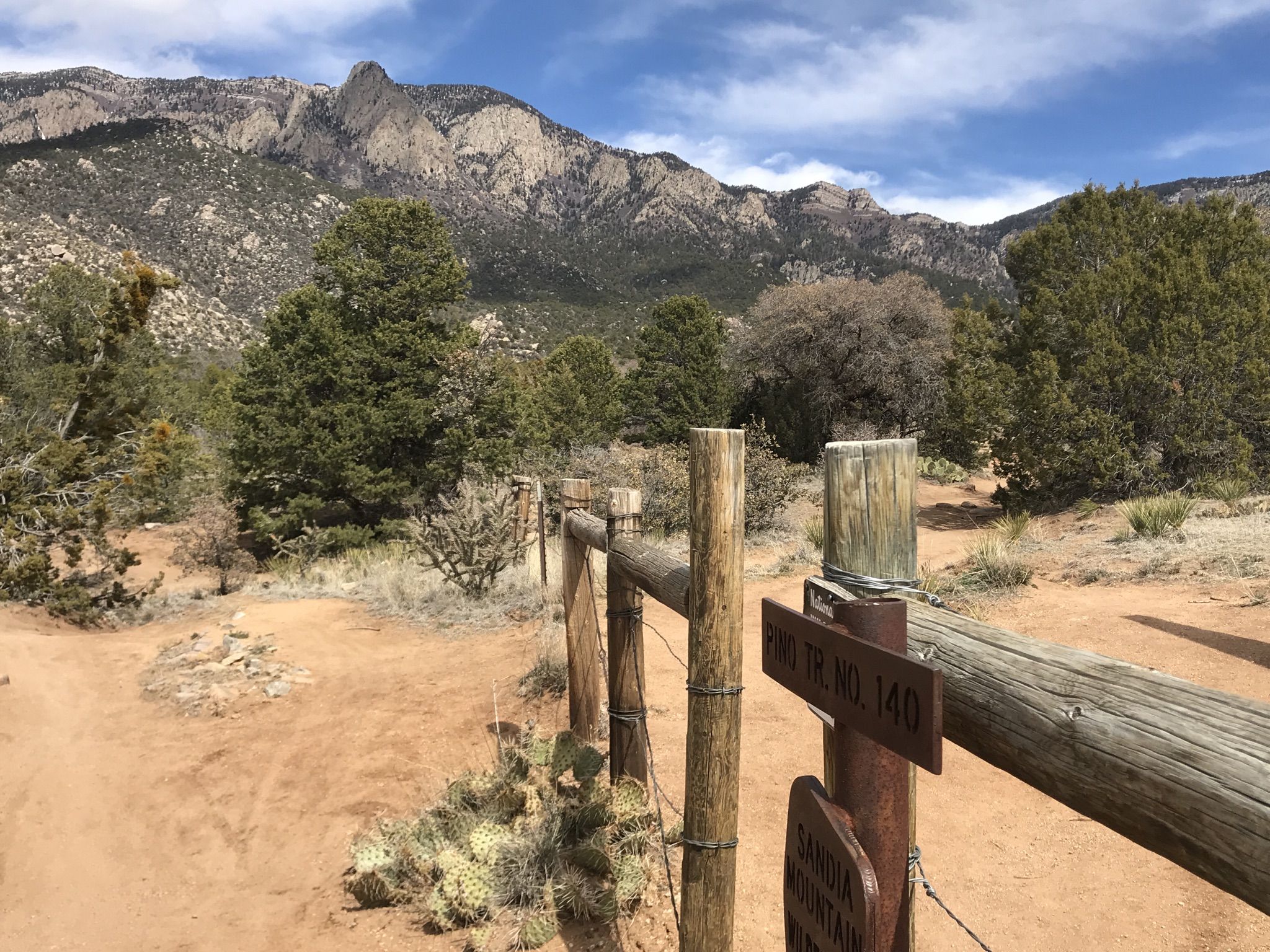 Dirt path leads to mountains under a bright sky, with a wooden fence. - Pino Trail
