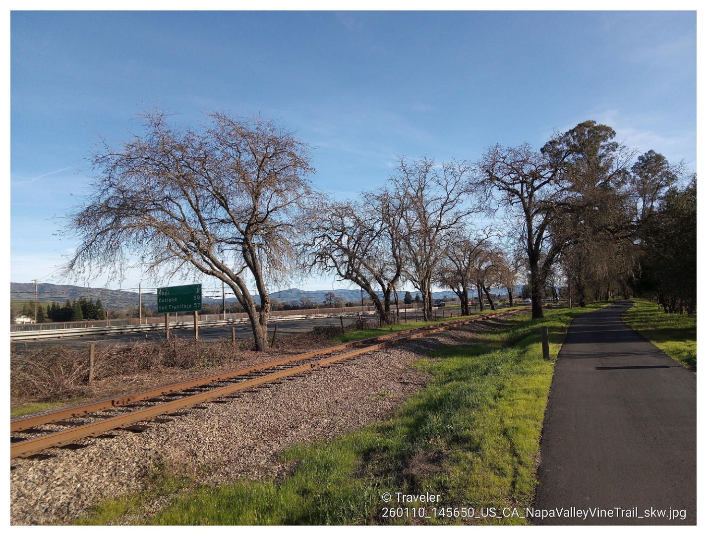 A paved path next to old railroad tracks, lined with bare trees. - Napa Valley Vine Trail – Andretti Winery loop from Oak Knoll