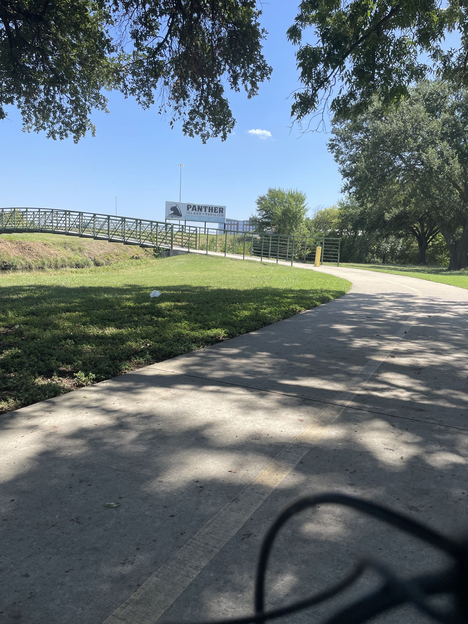 Paved path with shadows, green grass, and a distant bridge under sunny sky. - Trinity Trail Loop
