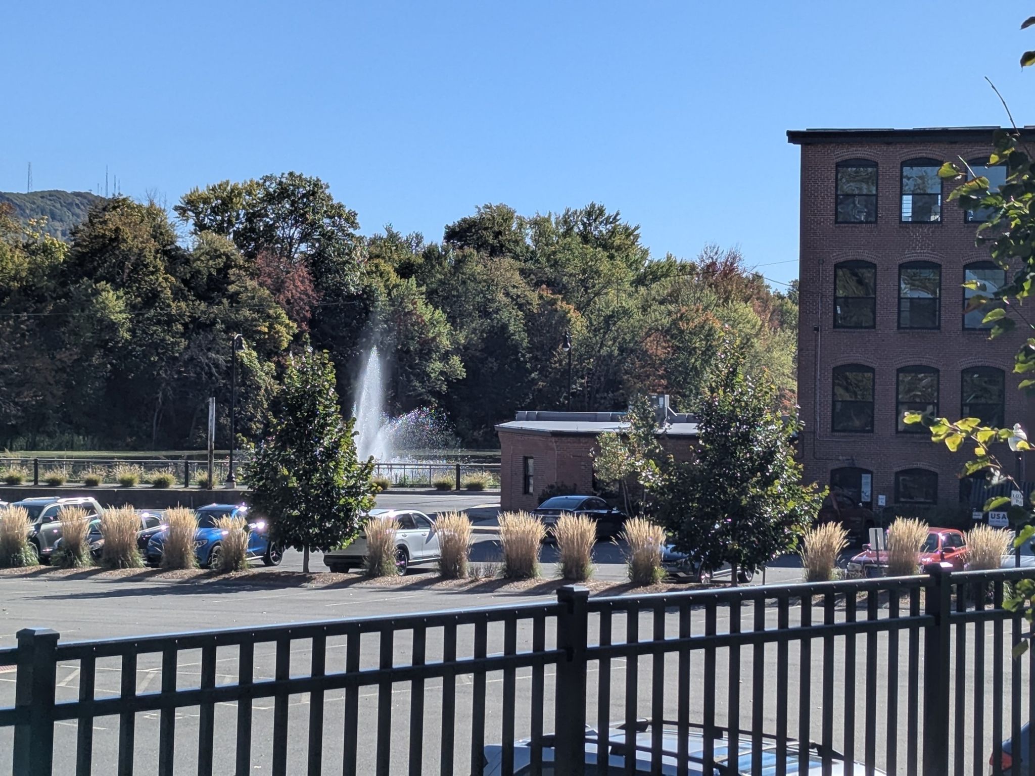 Fountain spraying water near a parking lot and brick building on a sunny day. - Arcadia Wildlife Sanctuary – Rubber Thread Pond loop from Northampton