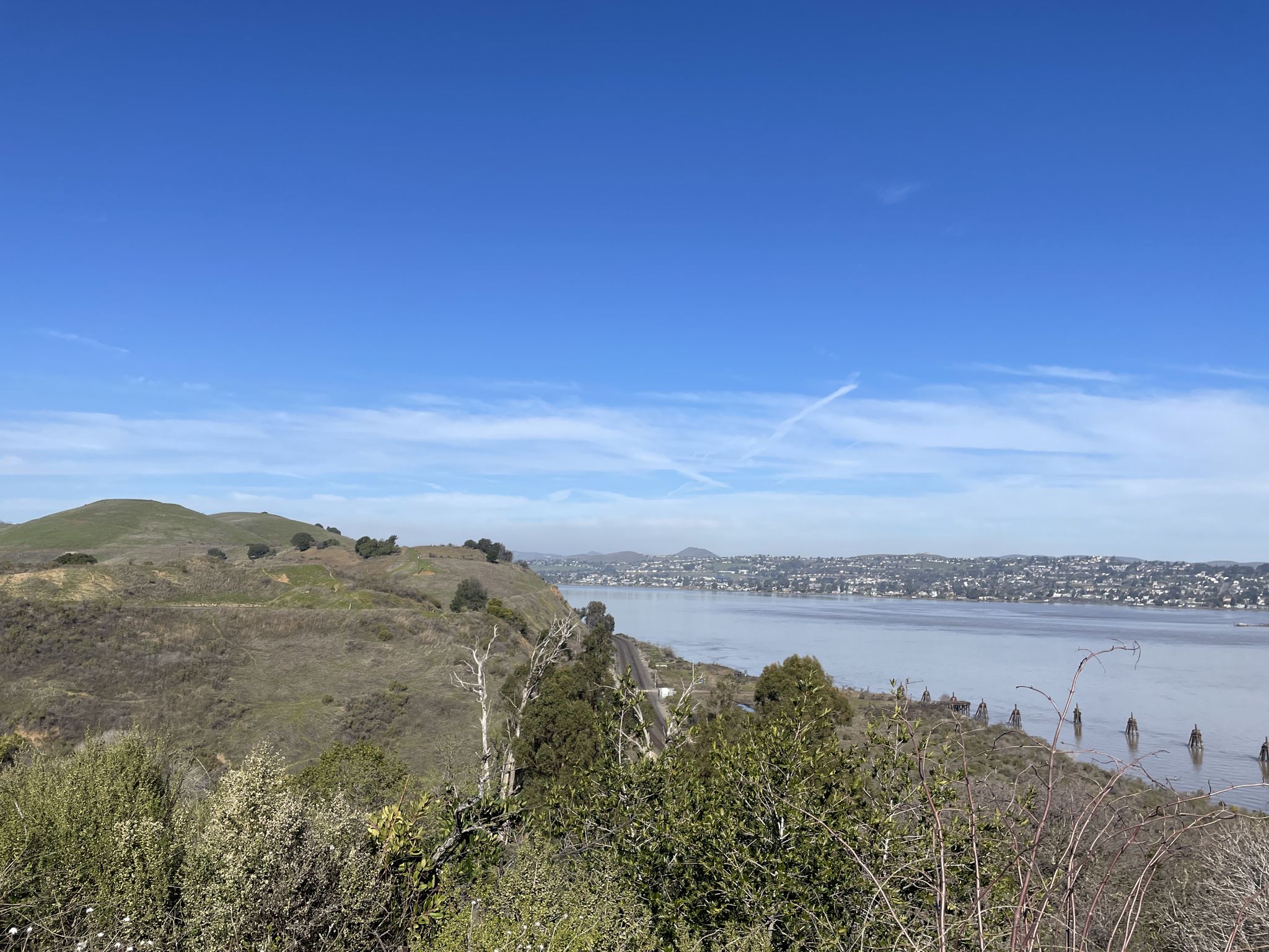 Wide view of a calm bay, green hills, and distant city under blue sky. - Carquinez Scenic Drive through – Carquinez Bridge loop from Martinez
