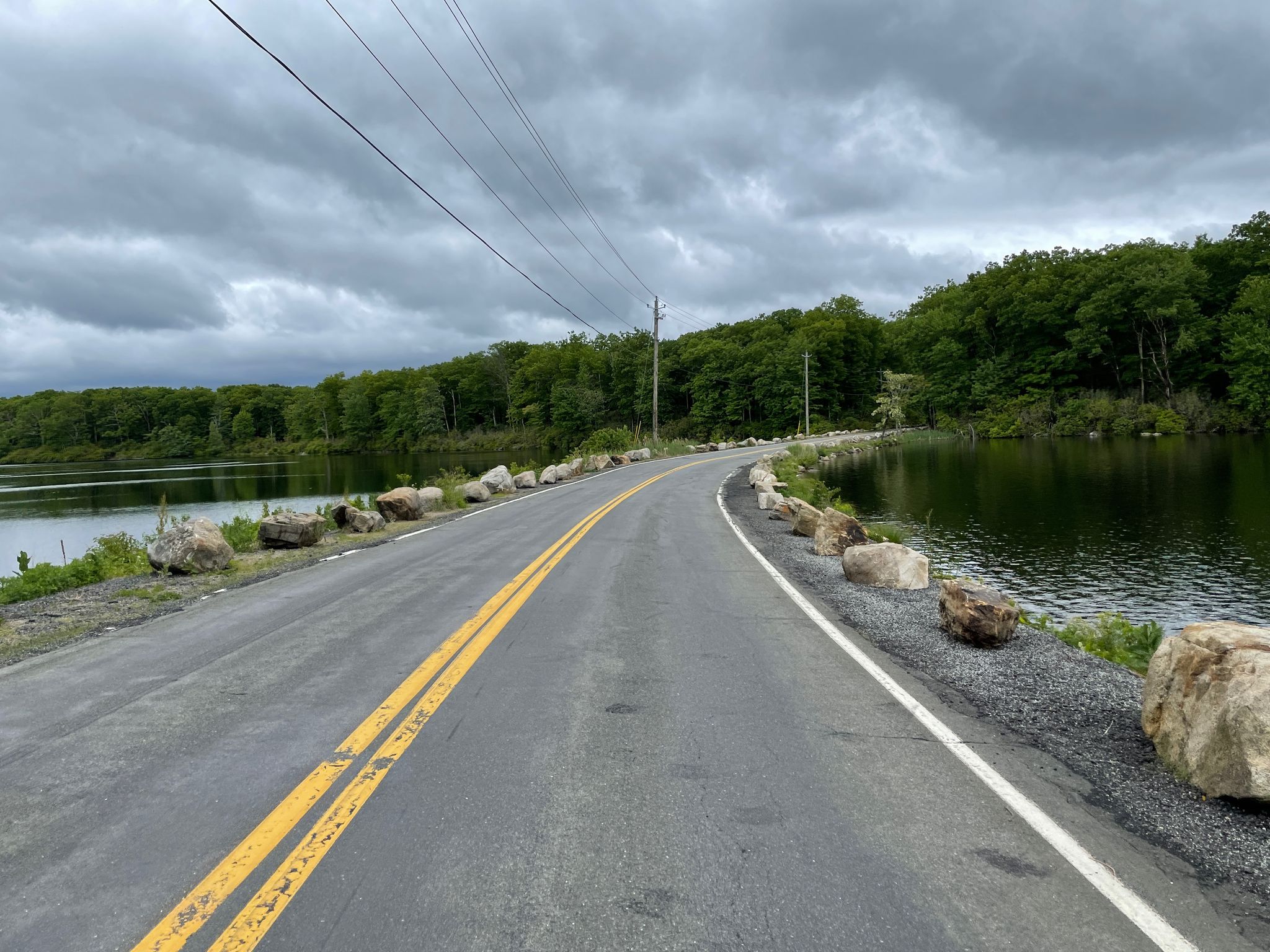 Curved road alongside a lake with forested hills under an overcast sky. - Lake Tiorati – Lake Welch Beach loop from Jackie Jones Mountain