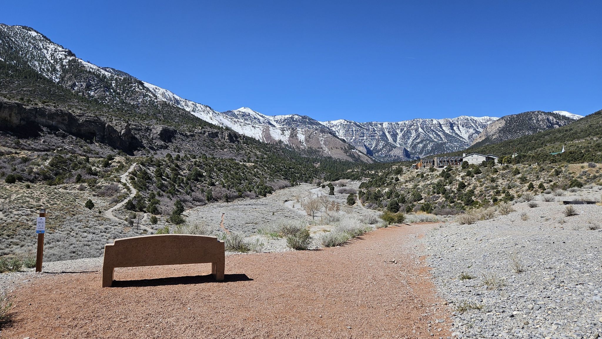 A wooden bench on a dirt path overlooking a valley with snow-capped mountains. - Escarpment Trail Loop