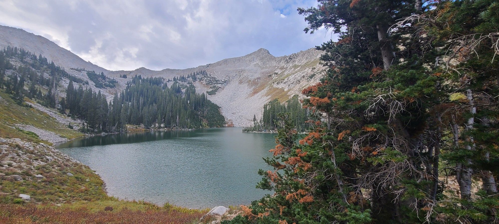 Mountain lake surrounded by rocky slopes and evergreen trees under a cloudy sky. - Red Pine Trail