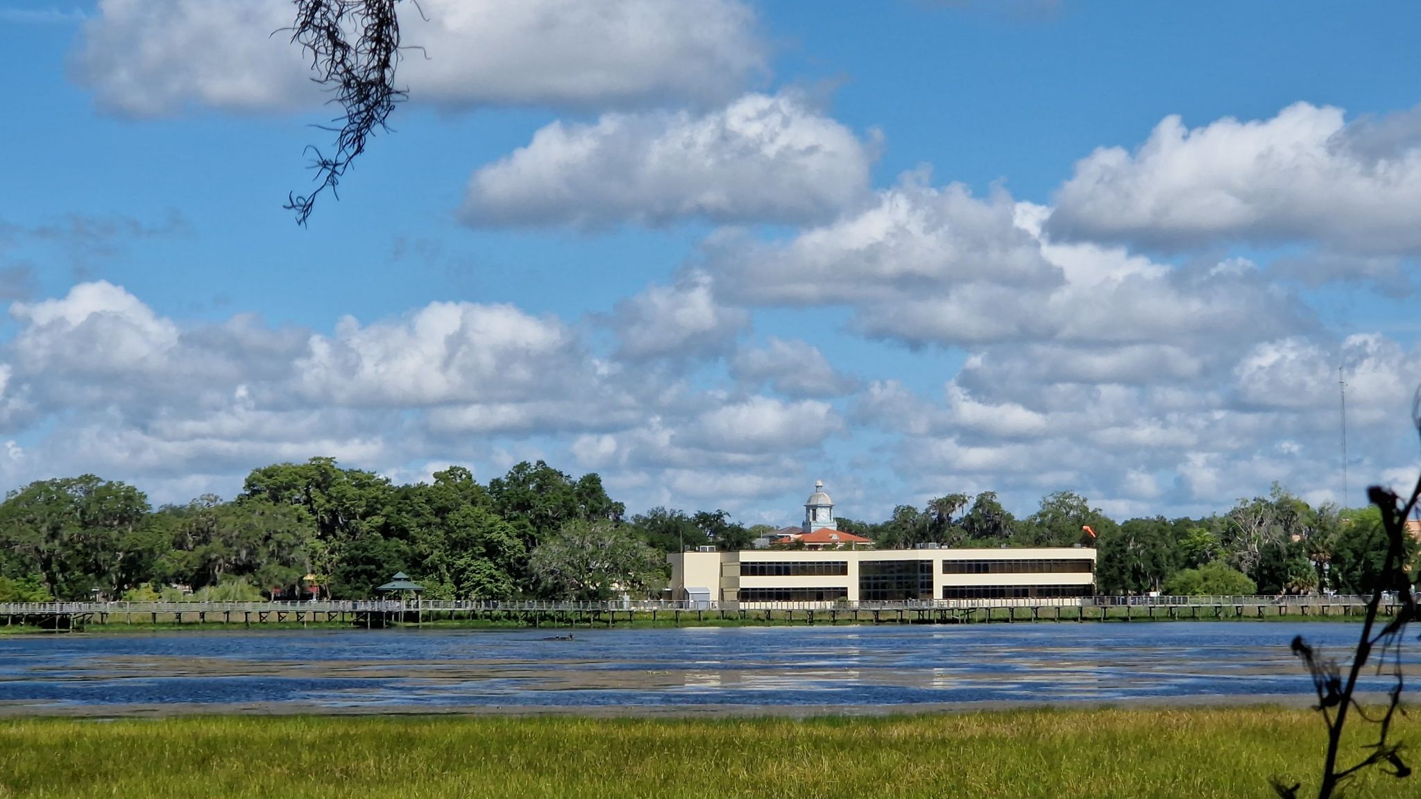A modern building across a calm body of water under a cloudy sky. - Withlacoochee State Trail: Inverness and Floral City Loop