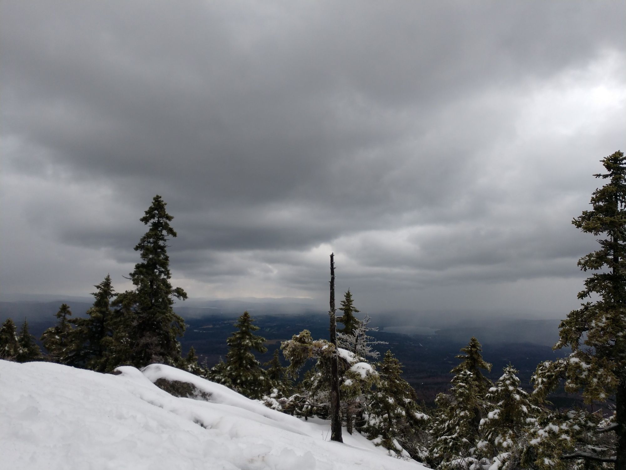 Snow-covered mountain landscape with evergreen trees under a dark, stormy sky. - Mount Kearsarge loop from Winslow State Park