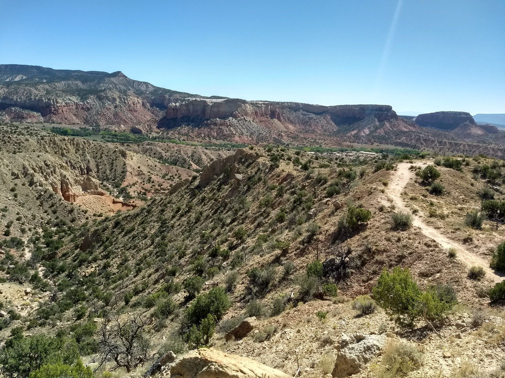 A winding dirt path overlooks a vast, arid canyon under a clear sky. - Chimney Rock Trail