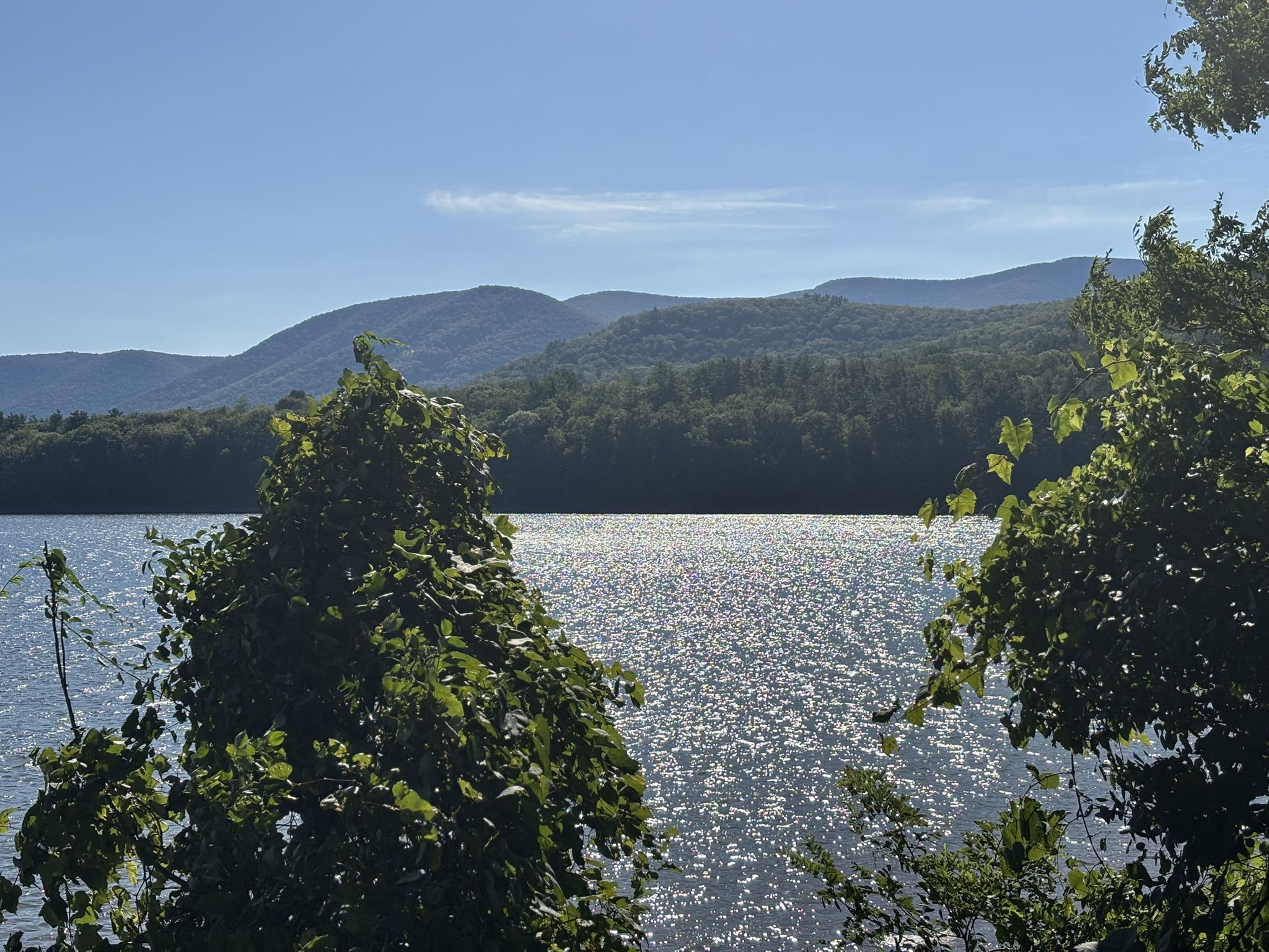 Sparkling lake under a bright sun, framed by green trees and distant mountains. - Frozen Ashokan Reservoir loop from Boiceville