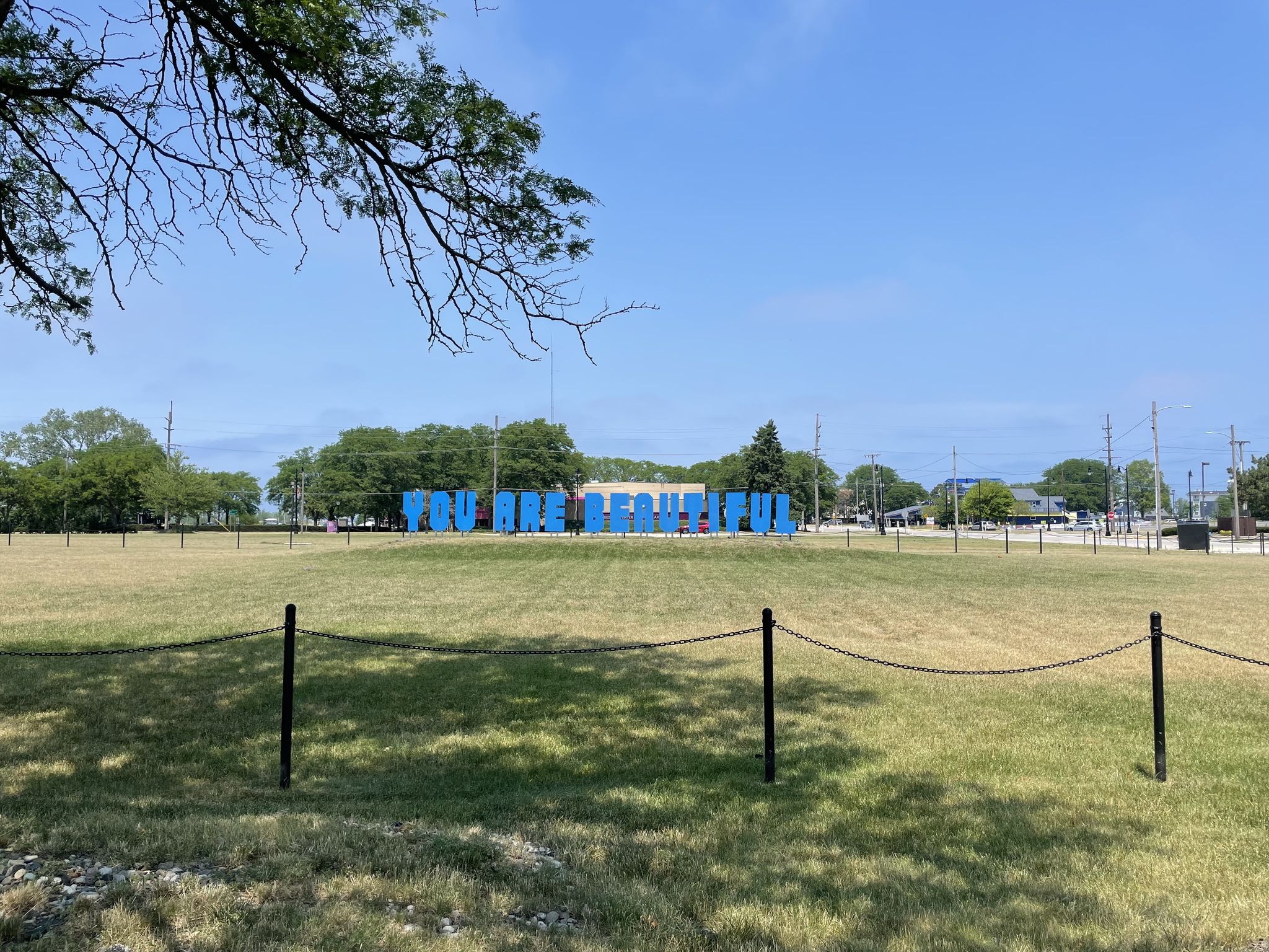 Large blue letters stand in a sunny grassy field with distant trees. - Singing Sands Trail Loop