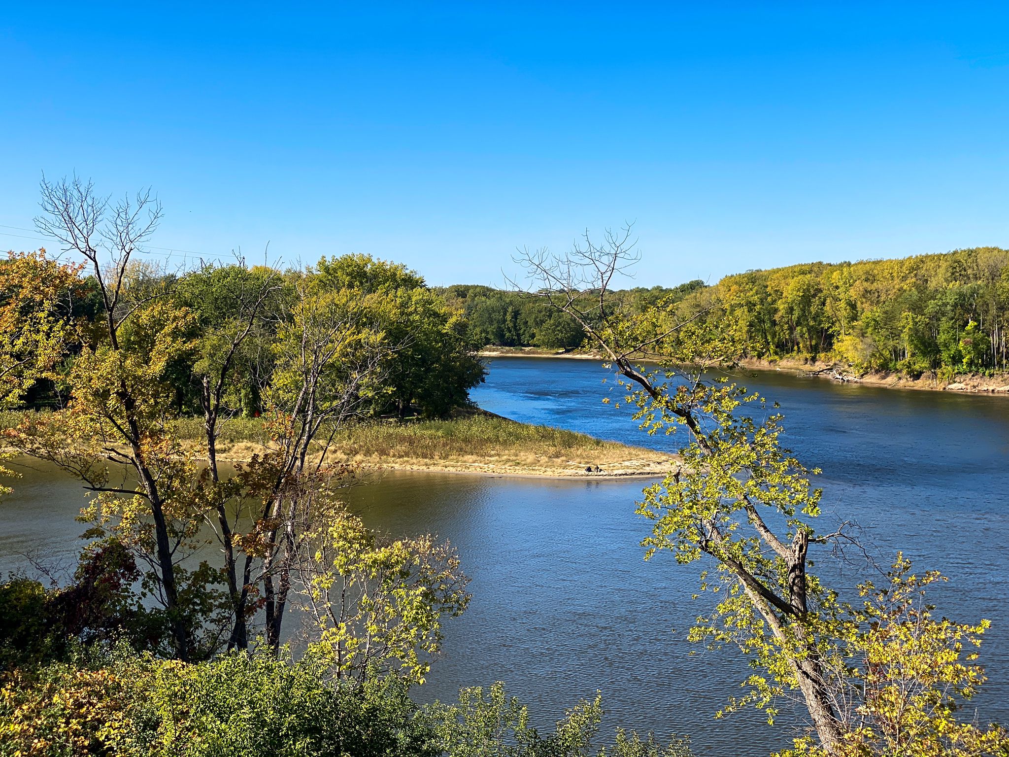 Wide river flowing through lush autumn trees under a clear blue sky. - Big Rivers Regional Trail