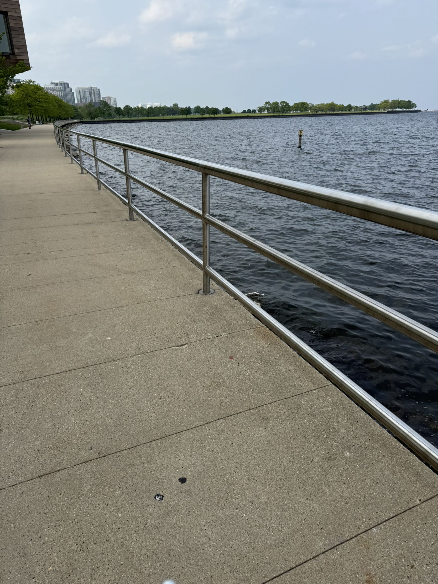 Concrete path with metal railing alongside water, distant city buildings. - Veterans Park Lagoon – Bradford Beach loop from Milwaukee