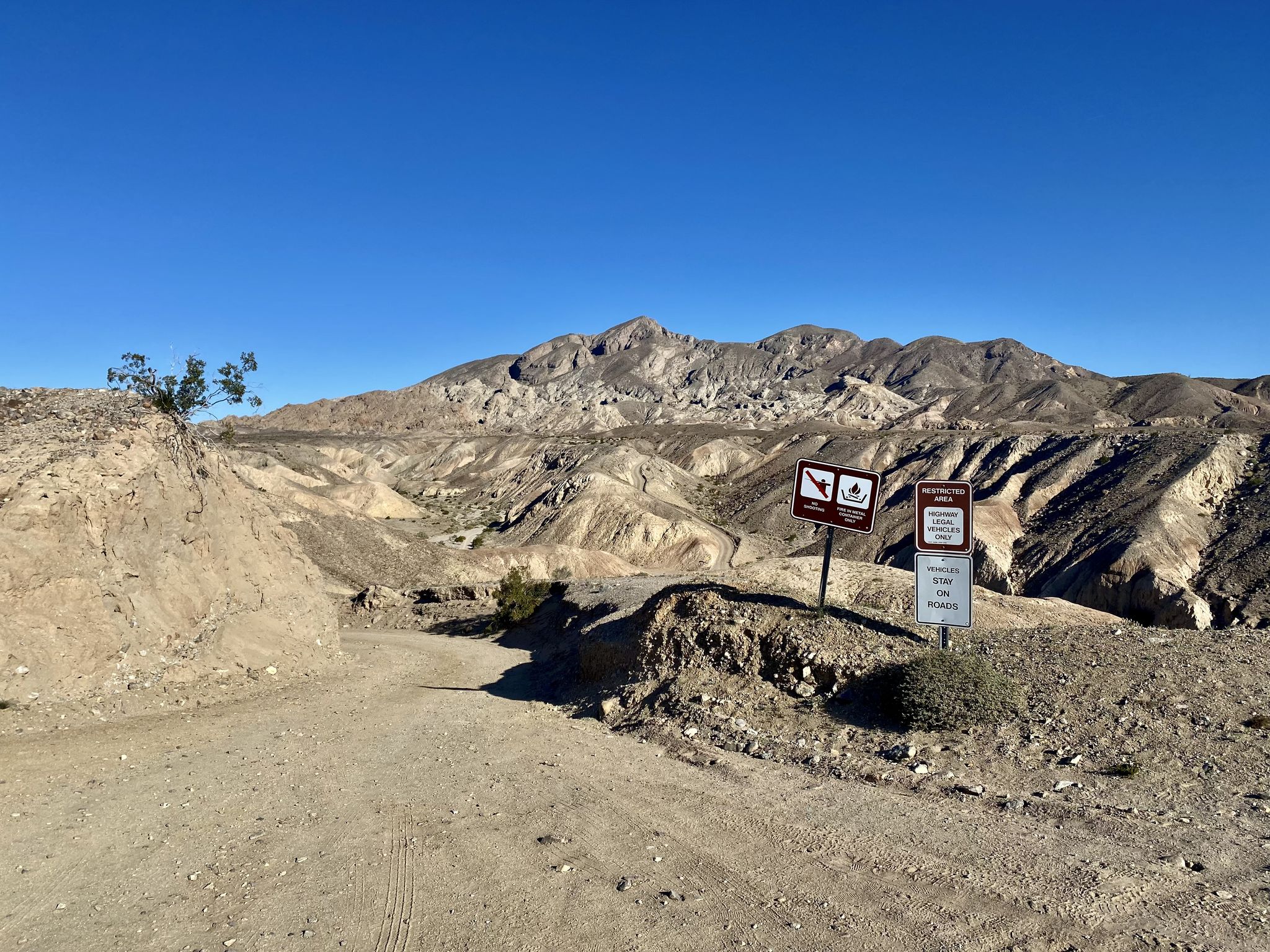 Dirt road leading into arid mountains with informational signs under clear sky. - Calcite Mine and Palm Wash Loop