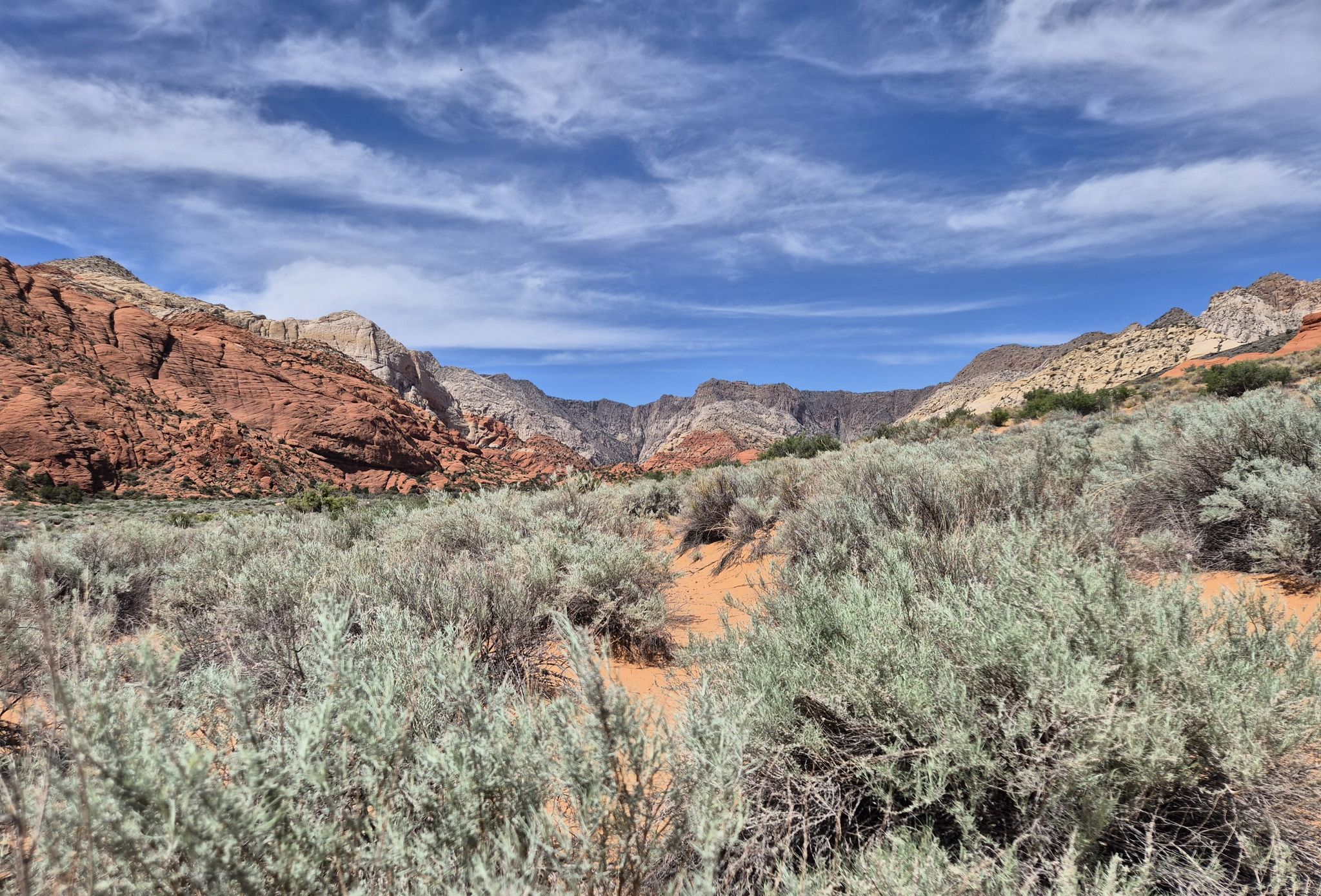 Desert landscape with red rock mountains, green brush, and a blue sky. - Lava Flow Trail