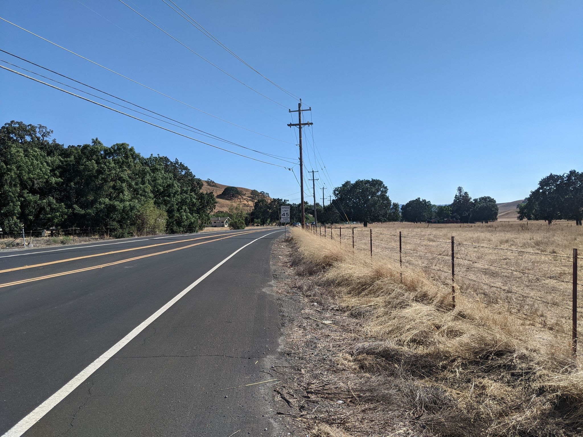 Paved road next to a dry field with a fence under clear blue sky. - Golf Ball Protection Tunnel – Museum of the San Ramon Valley loop from West Dublin/Pleasanton