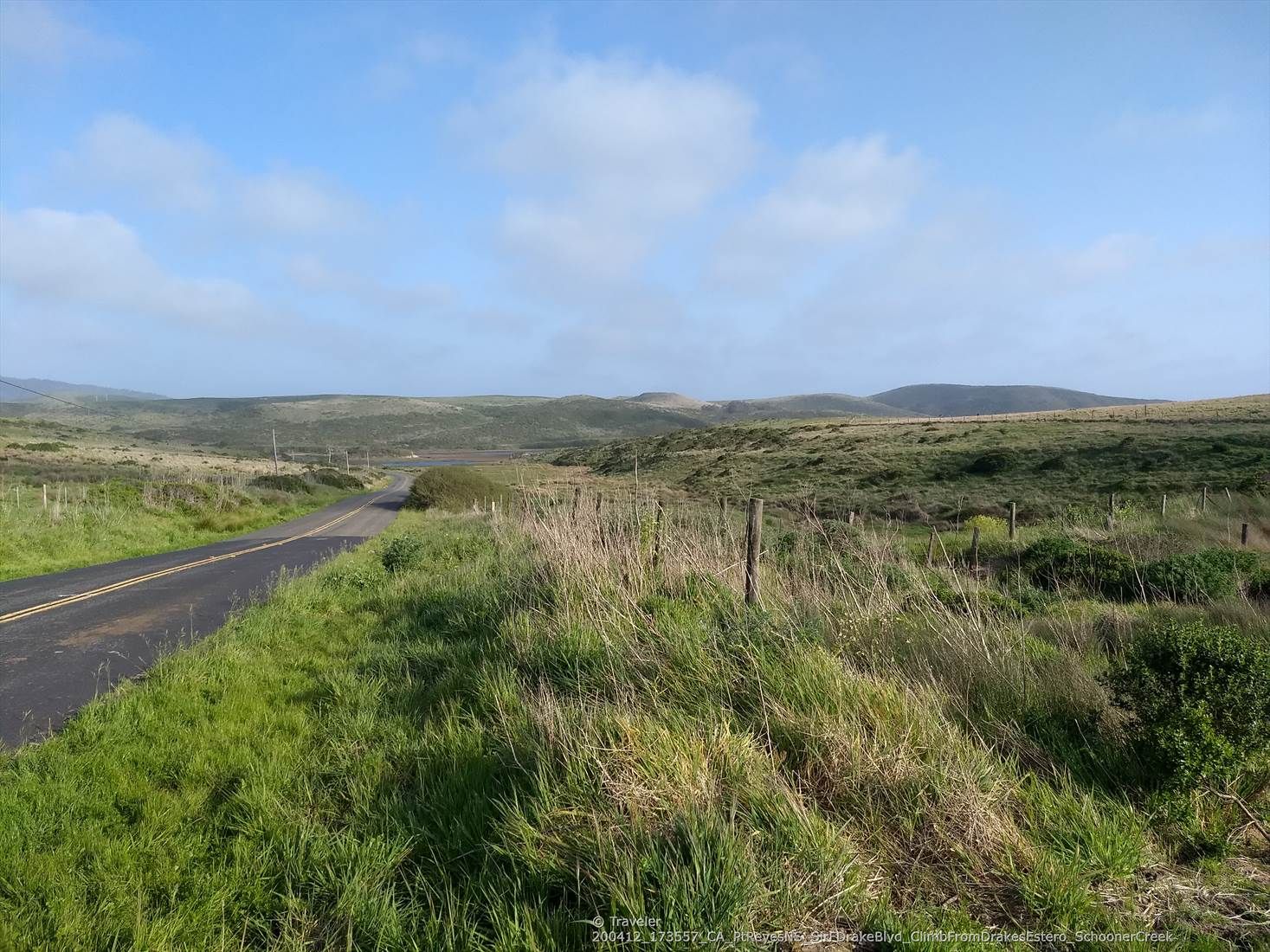 Paved road winding through rolling green hills under a bright, cloudy sky. - Sea Lion Overlook via Sir Francis Drake Blvd.