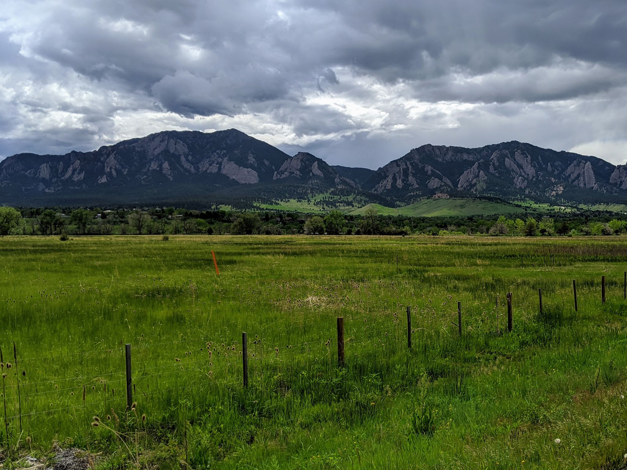 Dark mountains loom over a vast green field under cloudy skies. - Shanahan Hill – US 36 Bikeway loop from National Center for Atmospheric Research