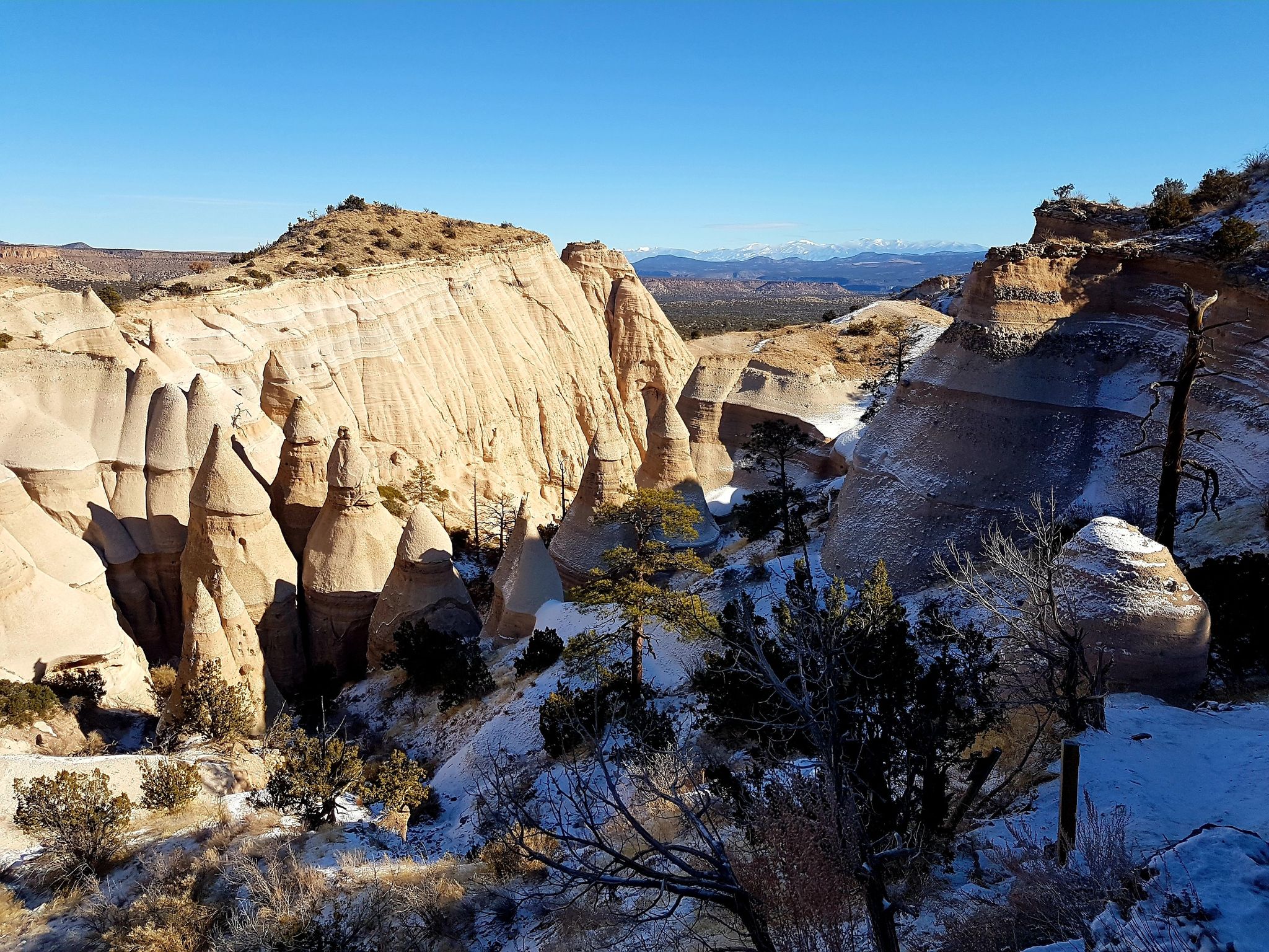 Snow-dusted canyon with light-colored rock formations and scattered trees under a clear sky. - Slot Canyon and Cave Loop Trail
