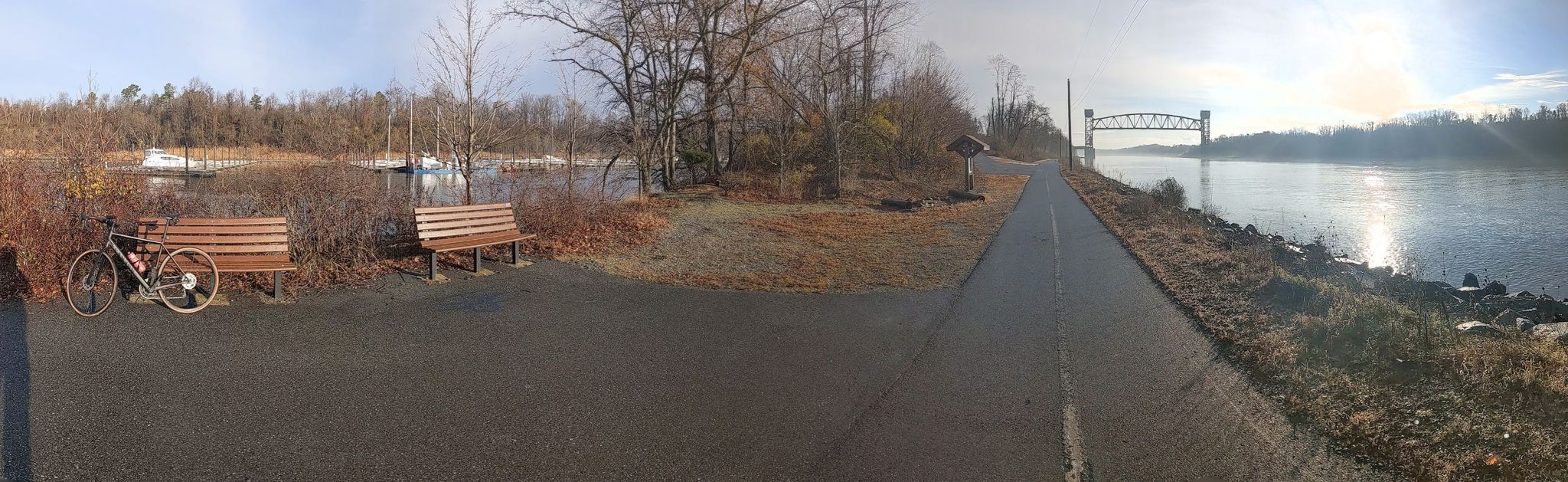 Panoramic view of a paved path, river, and parked bicycle on a bright day. - Mike Castle Trail – Summit Pointe loop from Summit Bridge